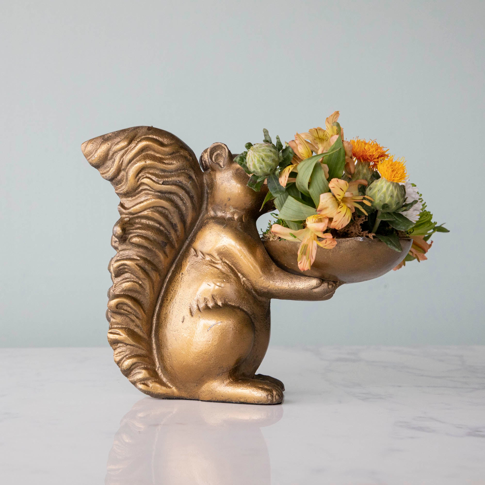 A bronze Accent Decor squirrel holding a bowl of flowers.