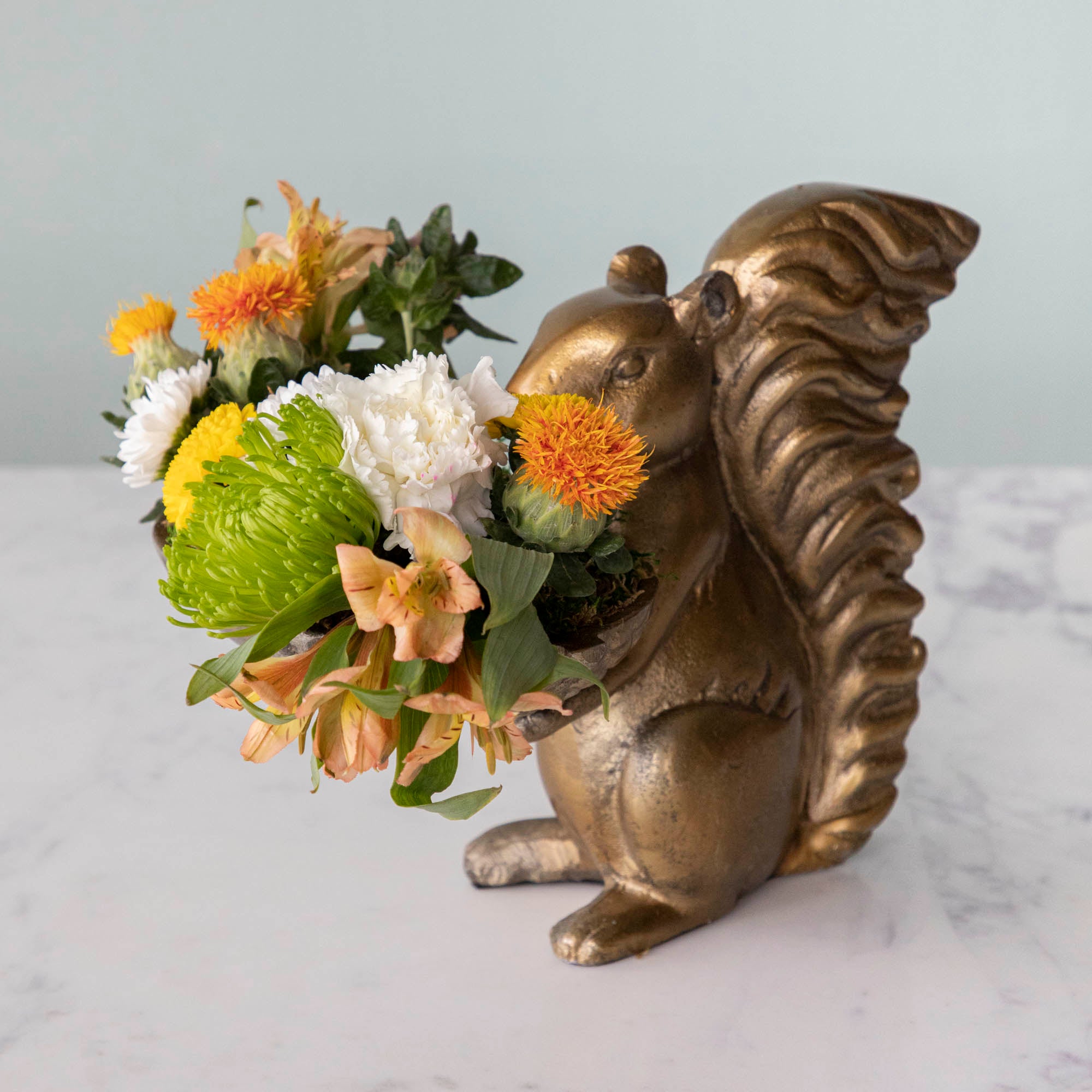 A bronze Accent Decor squirrel holding a bowl of flowers.