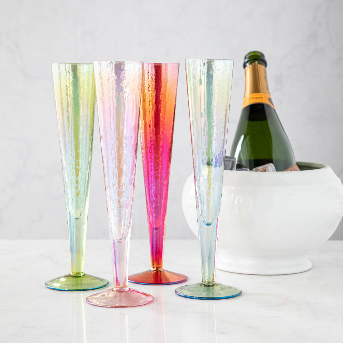Four Zodax Luster Slim Champagne Flute Glassware with a champagne bottle in an ice bucket in the background.