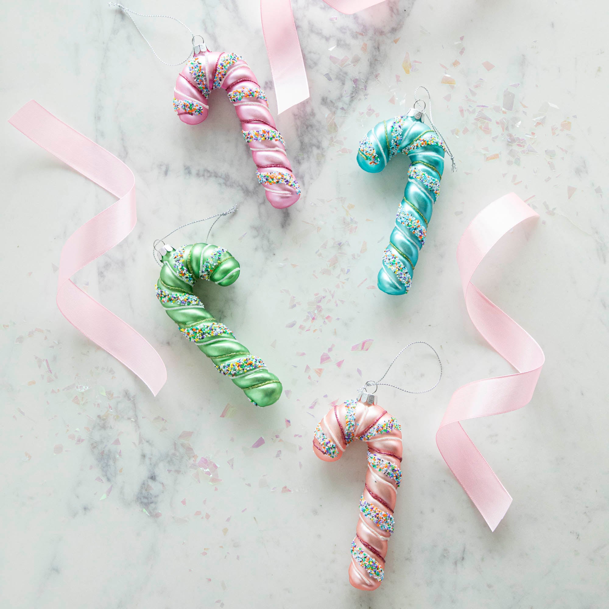 Four festive Glitterville candy cane ornaments on a marble table.