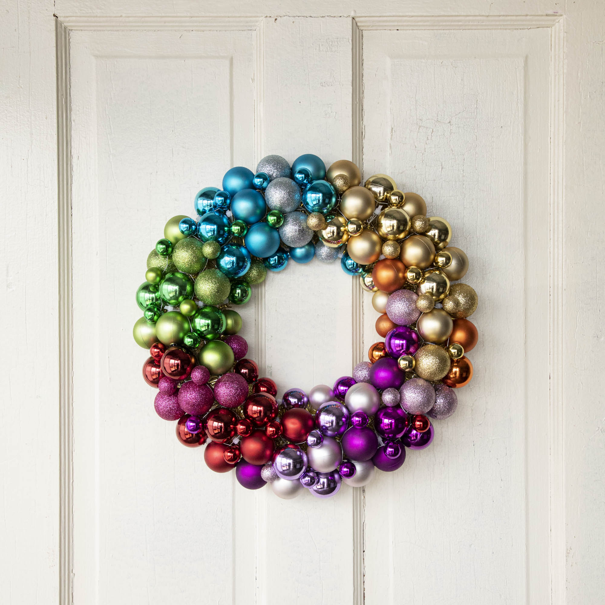 A multicolored wreath made of glass ornaments on a door.