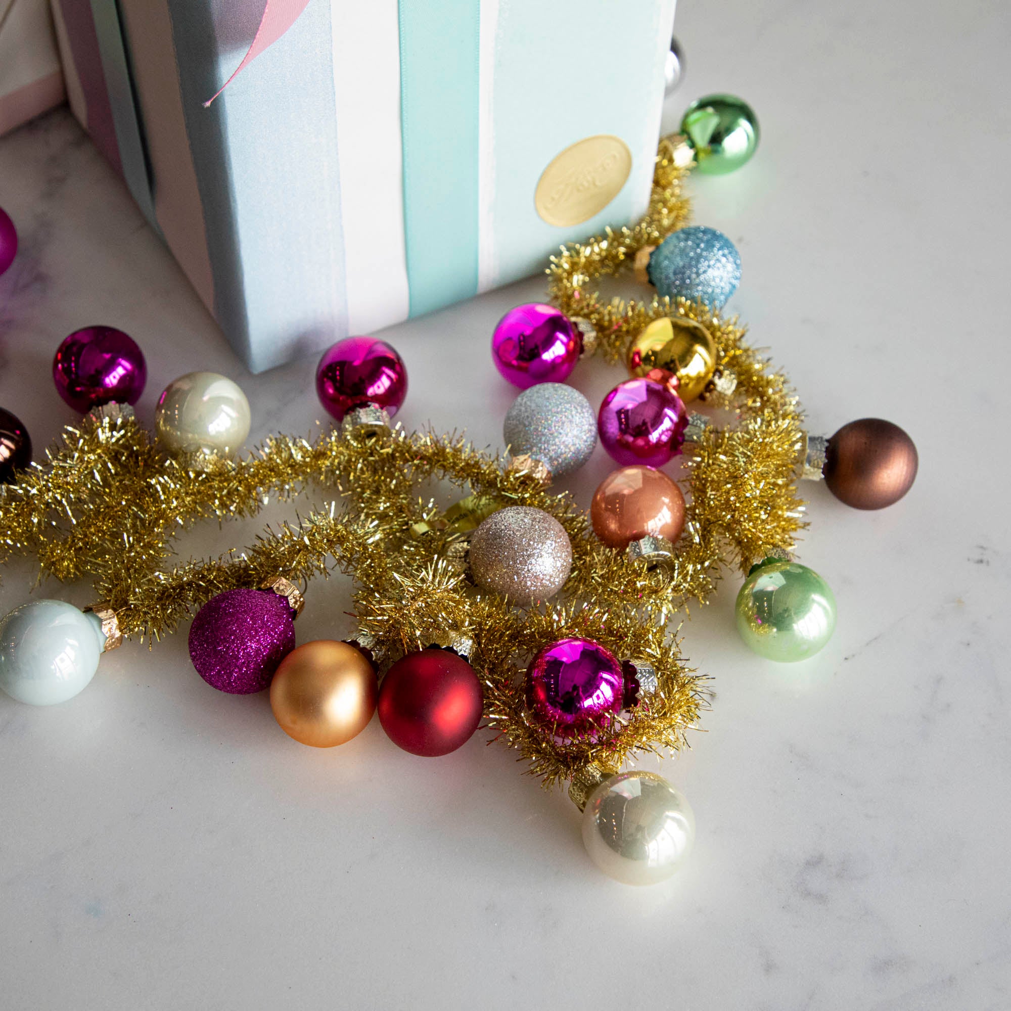 A garland made with gold tinsel string with multi colored balls attached to it strewn in front of 2 decorated gifts.