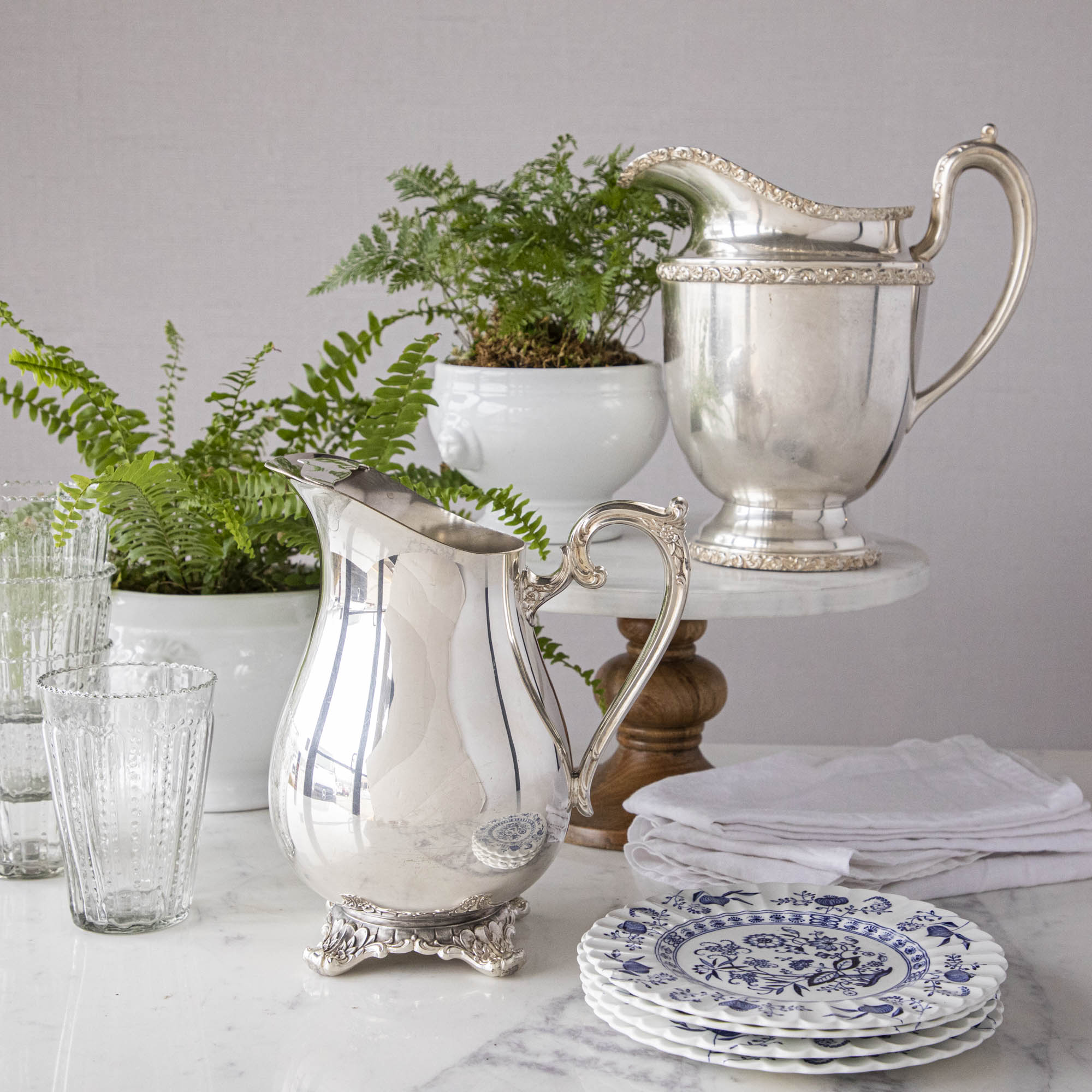 Elegant Hester & Cook vintage silver-plate water pitcher on a table adorned with glasses, plates, and a potted fern in the background.