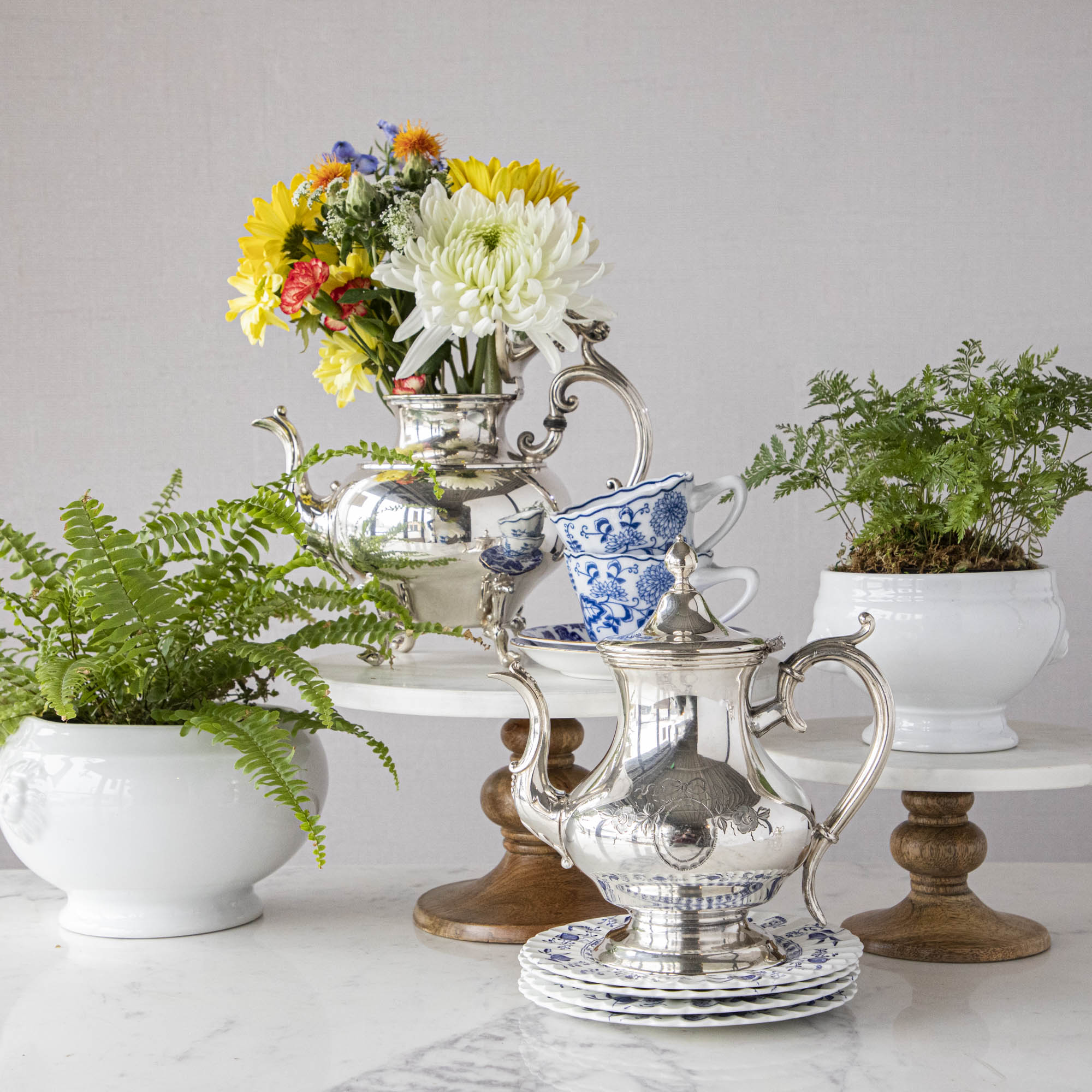 A blue and white table setting with a vase of tulips and Hester & Cook vintage silver-plated tea servers.