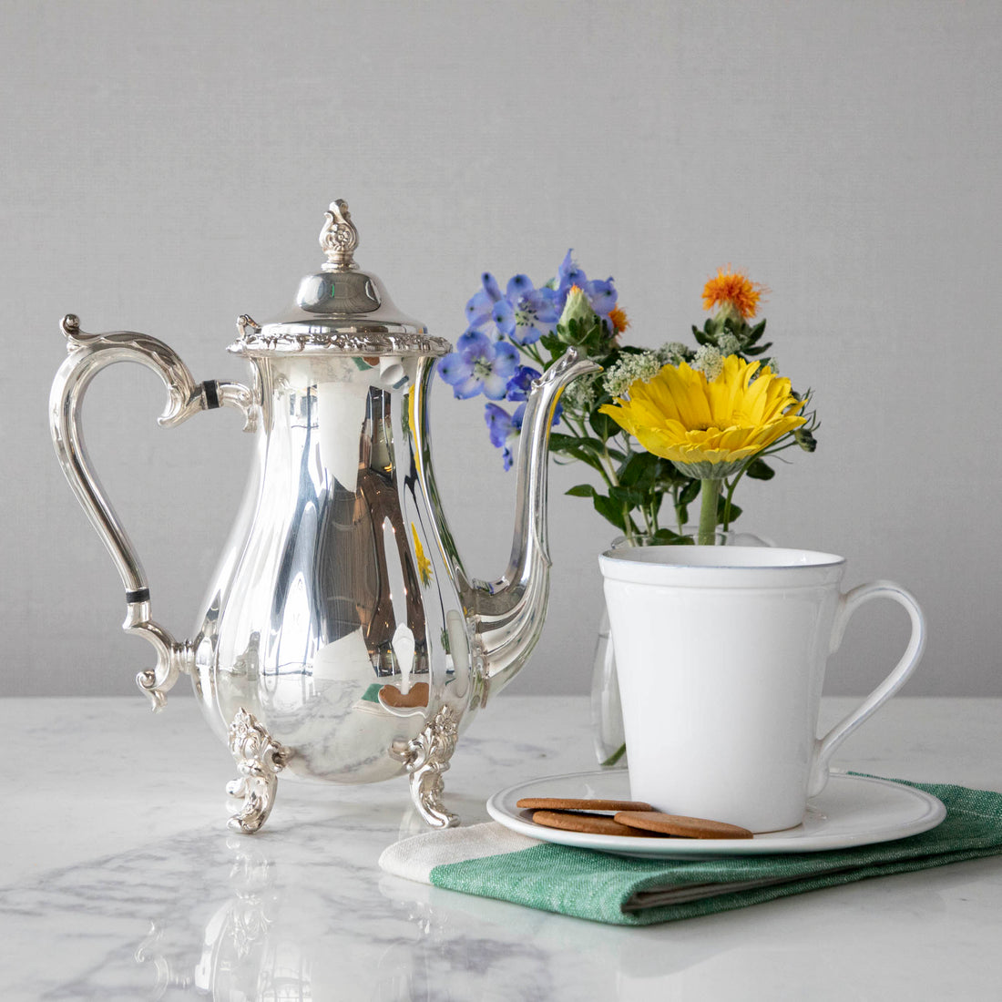 Hester &amp; Cook vintage silver-plate coffee server, white cup, and a bouquet of flowers on a marble countertop.