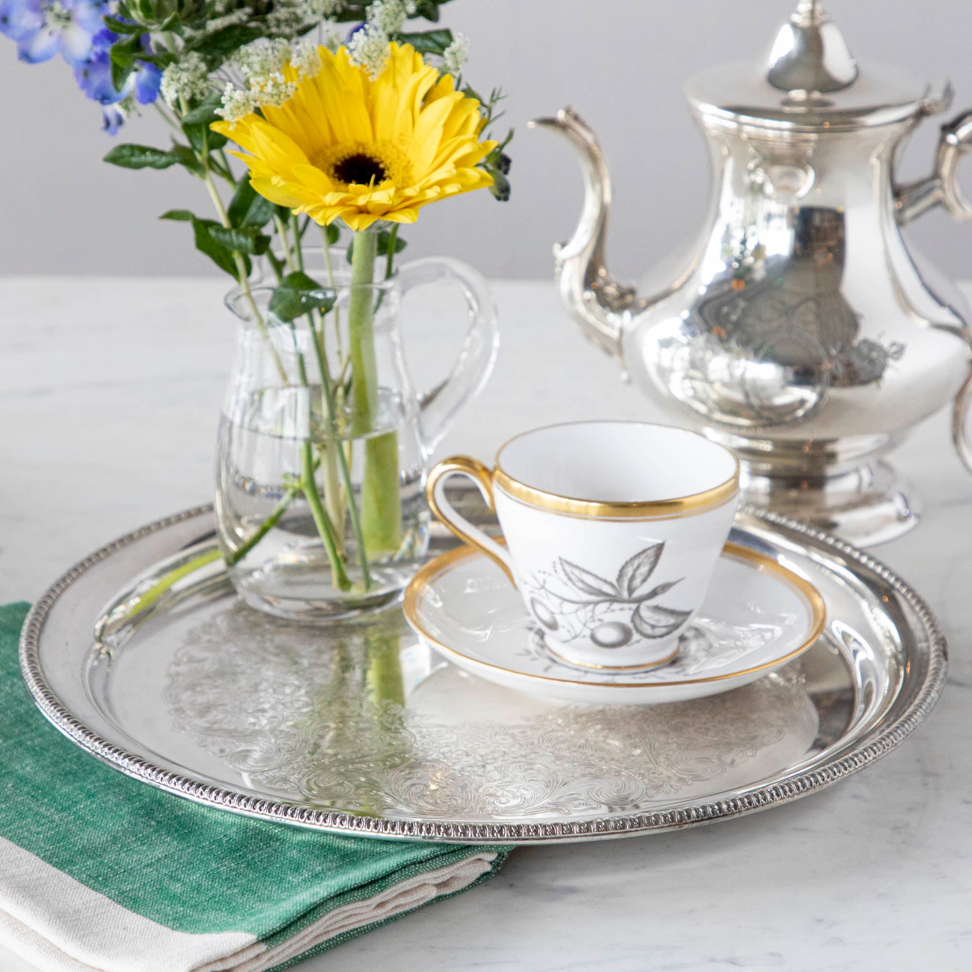A vintage silver-plate tray with a tea cup and a vase of flowers on it.