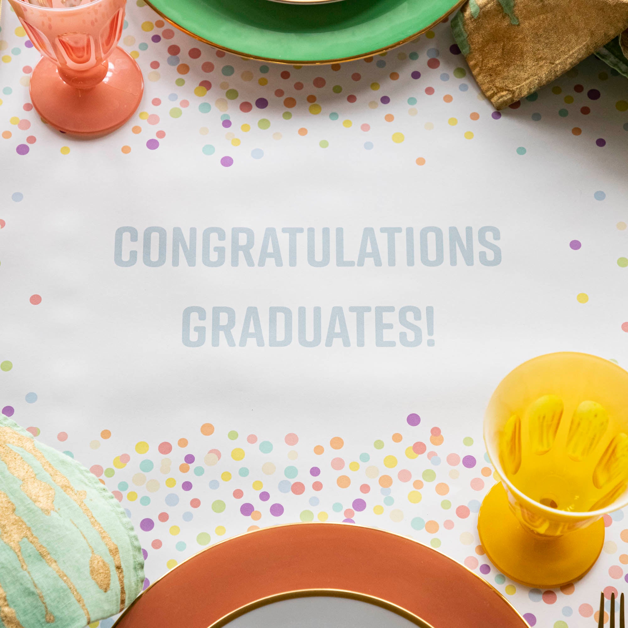 Close-up of the Confetti Sprinkles Personalized Runner under a festive table setting, with &quot;CONGRATULATIONS GRADUATES!&quot; printed in light blue.