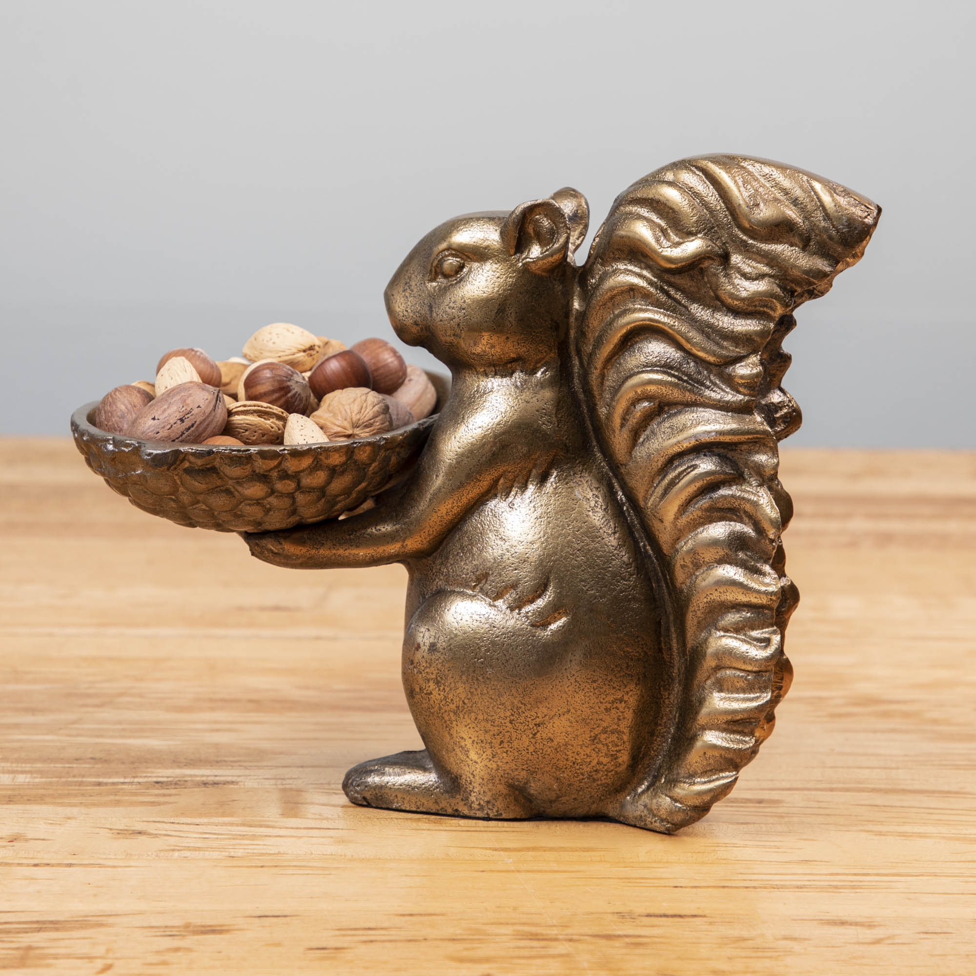 A bronze Accent Decor squirrel holding a bowl of nuts.