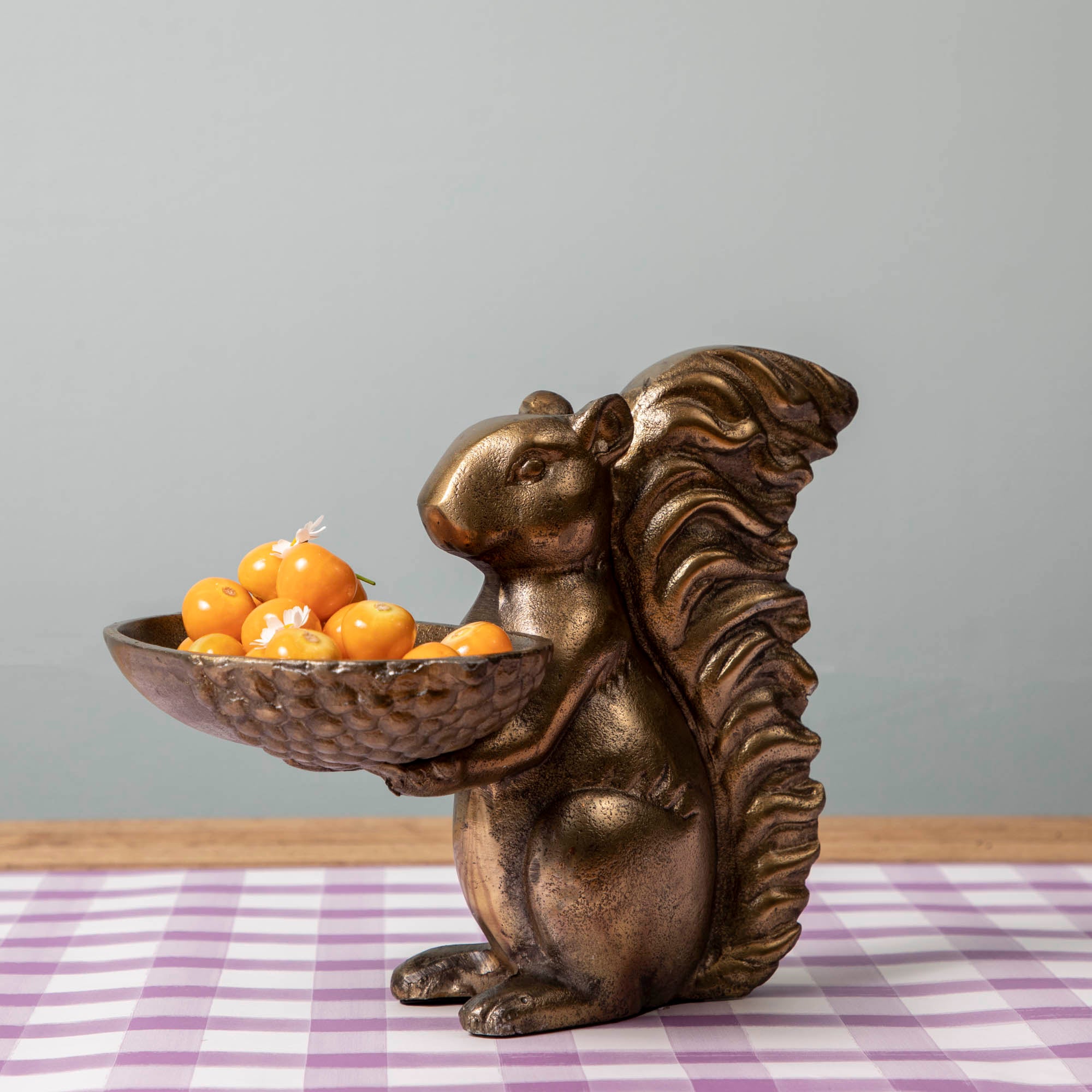 A bronze Accent Decor squirrel holding a bowl of tomatoes.