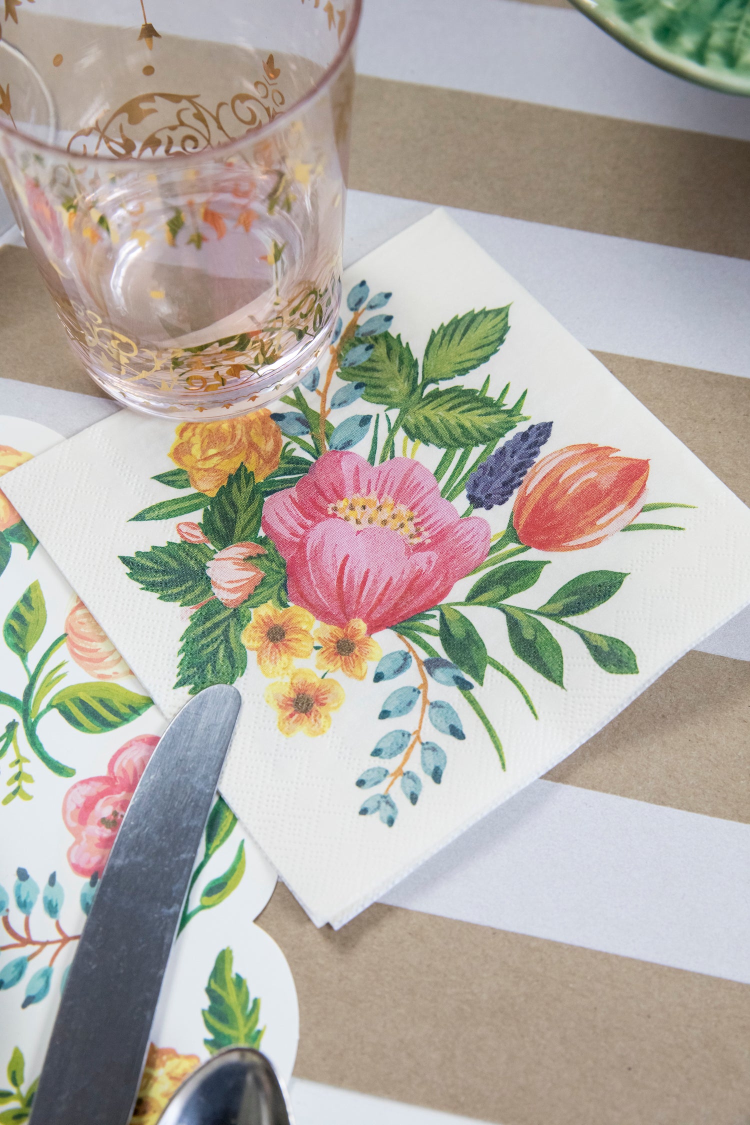 A Sweet Garden Cocktail Napkin under a glass of water in a floral place setting.