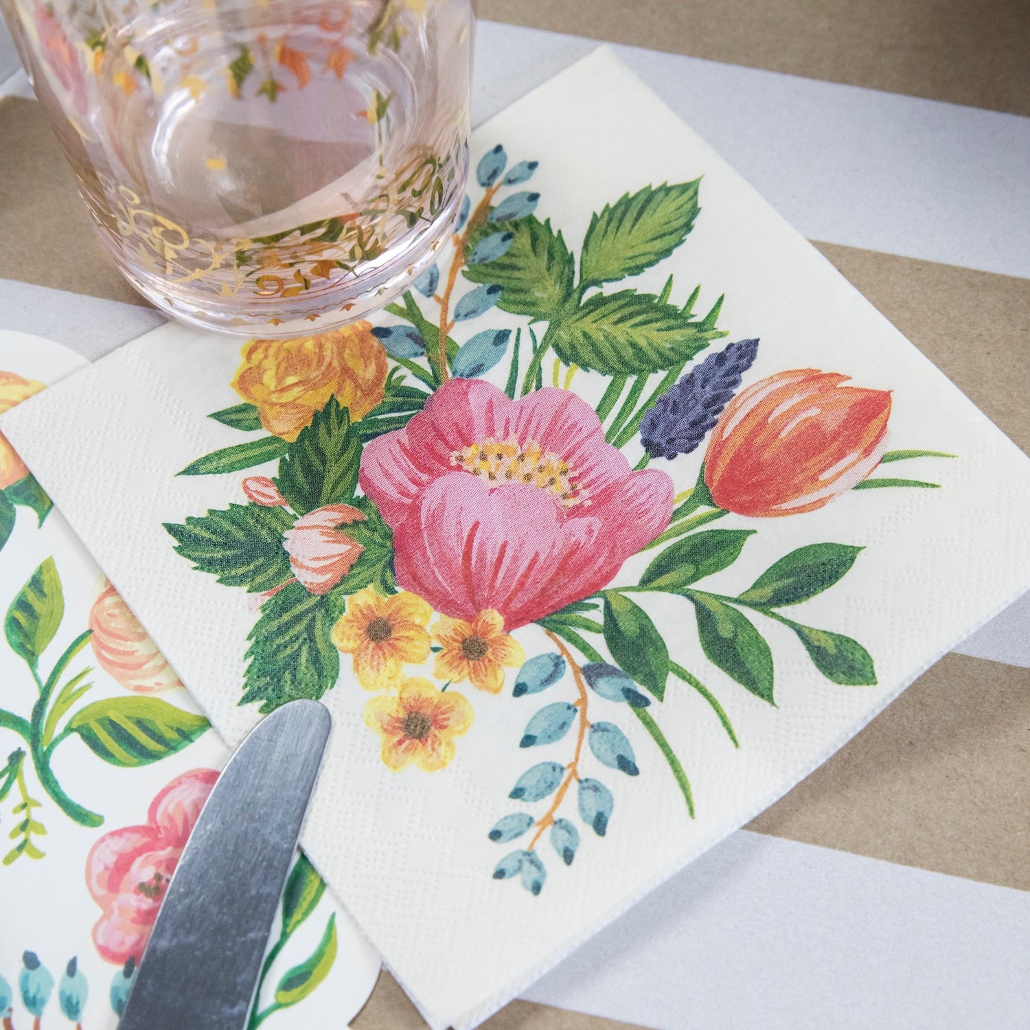 A Sweet Garden Cocktail Napkin under a glass of water in a floral place setting.