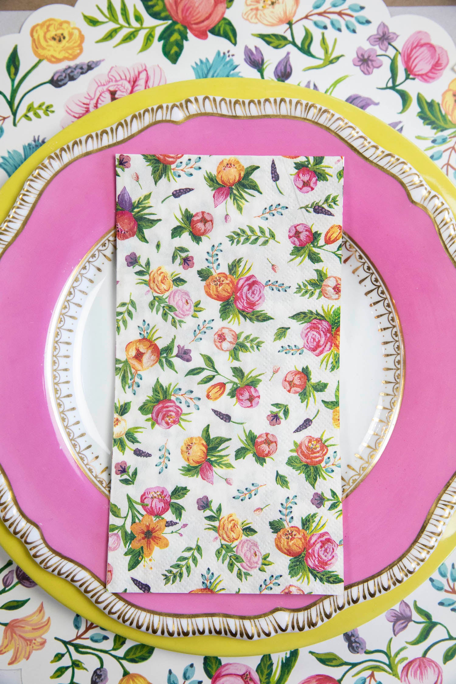 A Sweet Garden Guest Napkin centered on the pink and yellow plate in a floral place setting.
