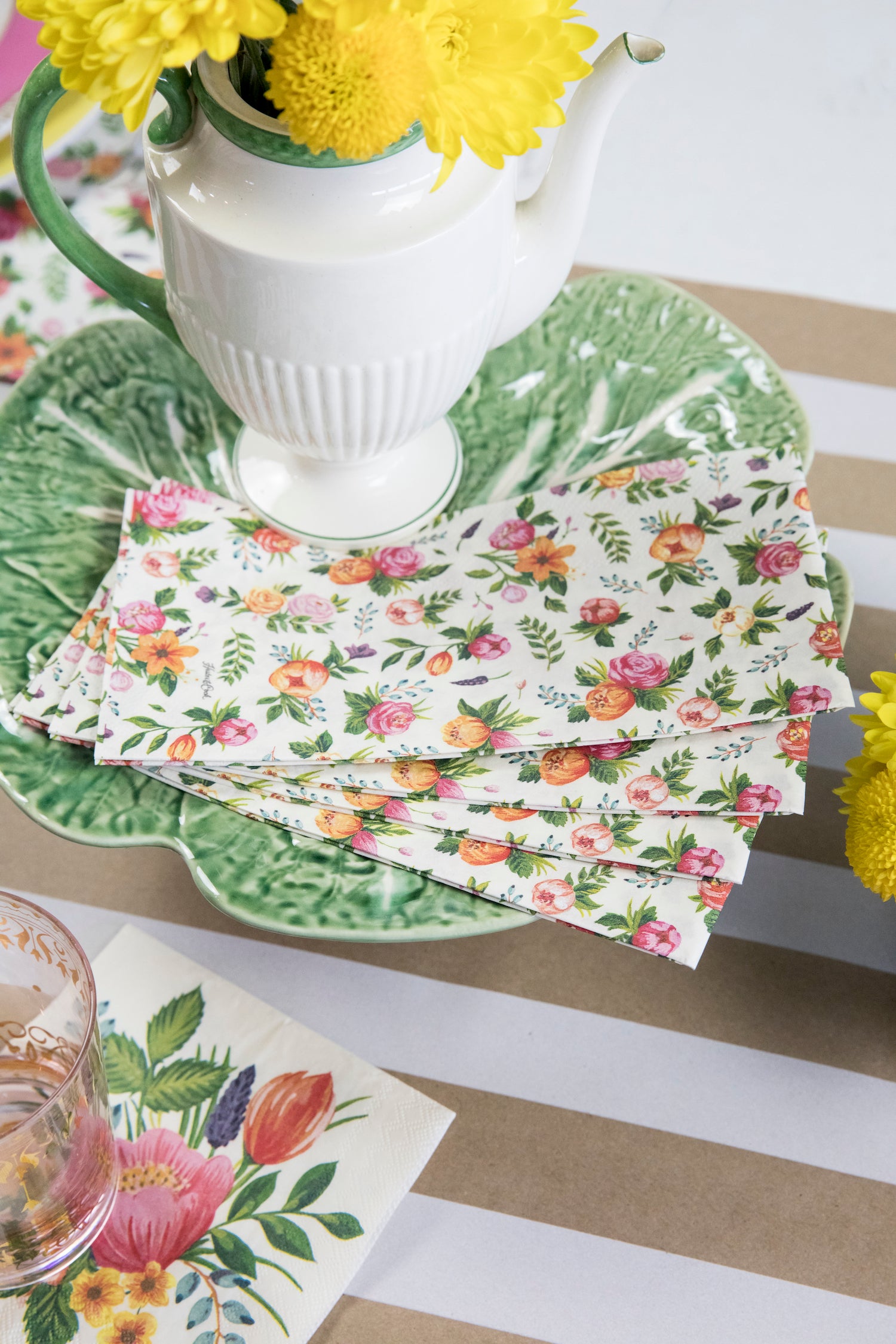 Four Sweet Garden Guest Napkins fanned out on a green plate in a floral table setting.