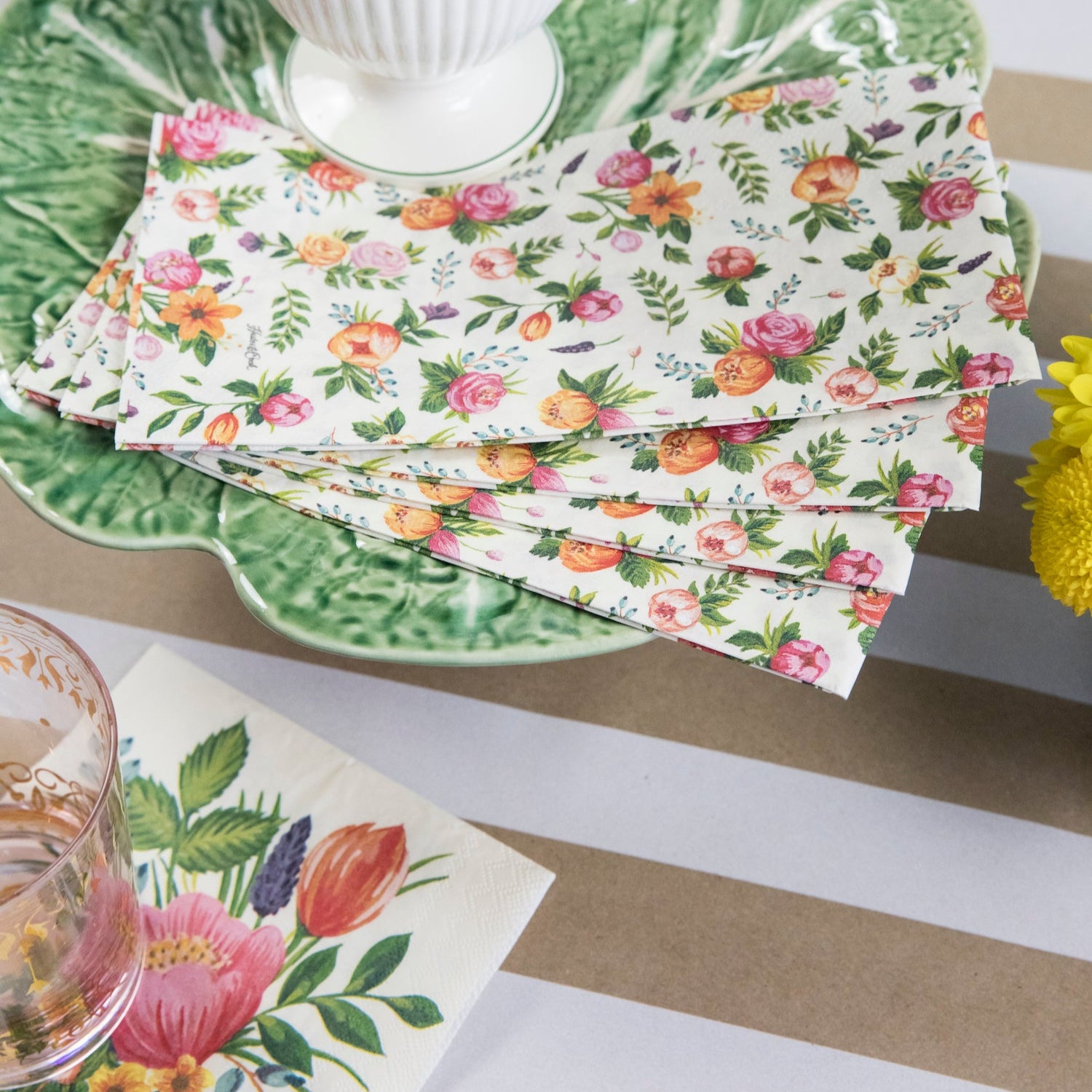 Four Sweet Garden Guest Napkins fanned out on a green plate in a floral table setting.