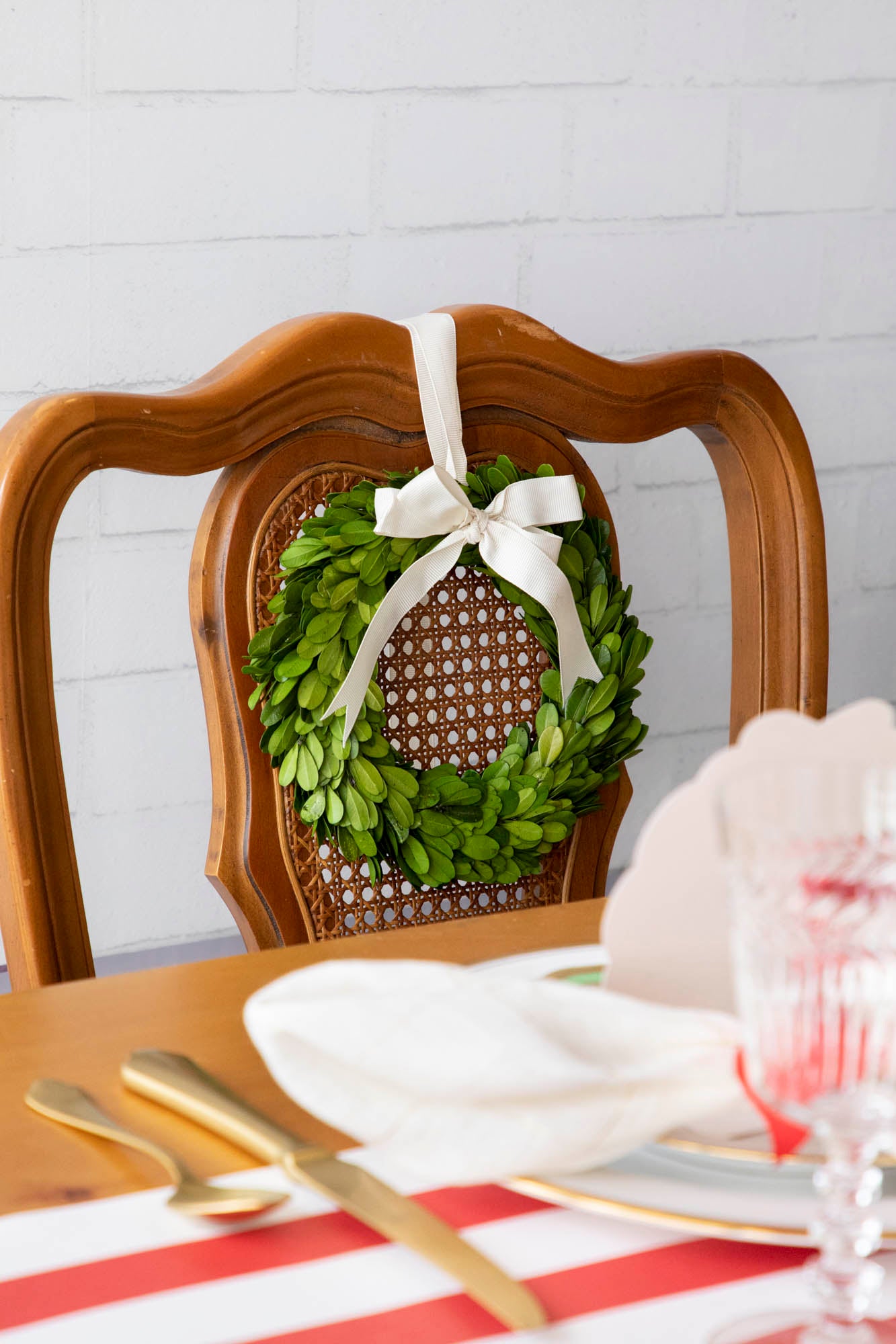 A fresh white chair adorned with a vibrant green Boxwood Wreath with Cream Grosgrain Ribbon from Porch View Home.