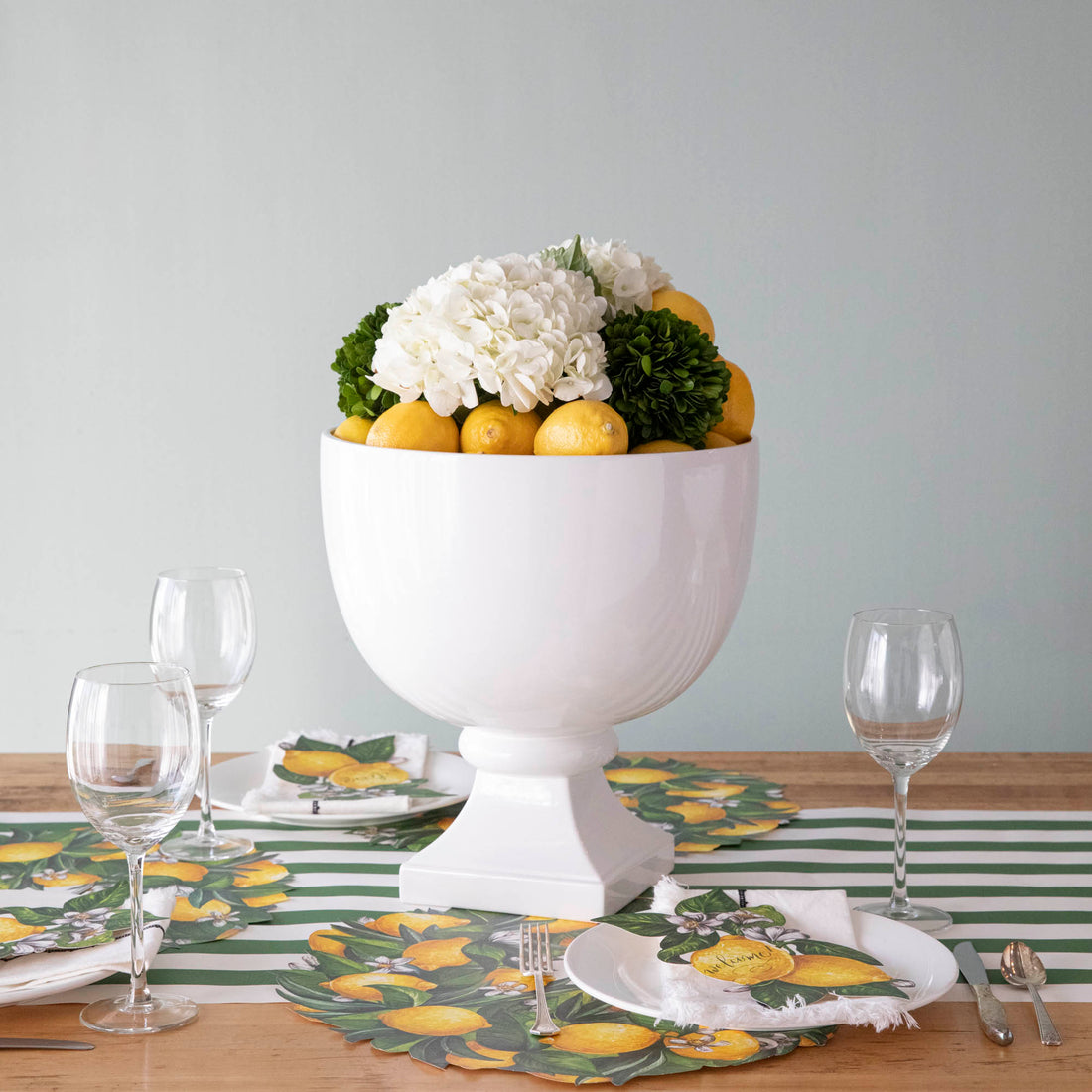 White European ceramic Pedestal Bowls from Park Hill, decorative centerpiece on pedestals, one filled with lemons and flowers, on a striped surface with wooden board.