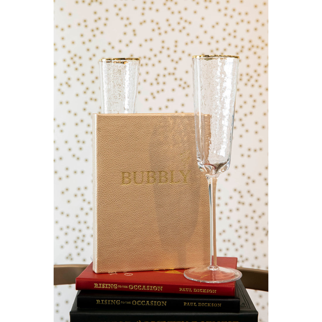 Two Bubbly glasses and a book with &quot;sparkling cocktails&quot; on the cover, placed on top of another book against a polka-dotted background. (Graphic Image)