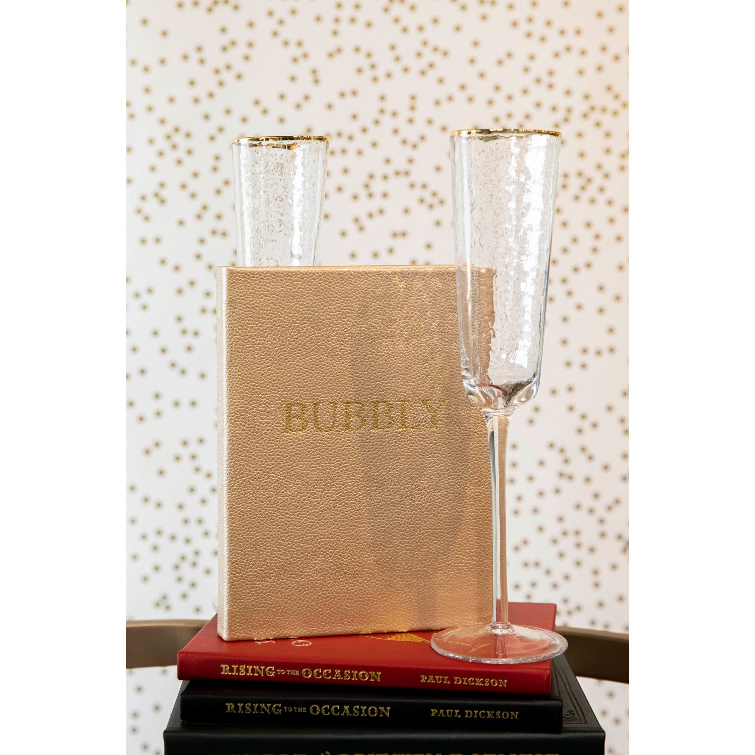 Two Bubbly glasses and a book with "sparkling cocktails" on the cover, placed on top of another book against a polka-dotted background. (Graphic Image)
