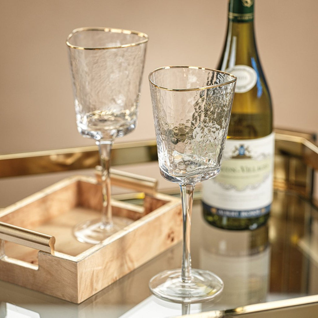Two Zodax Hammered Glasses with Gold Rim on a tray with a bottle of champagne in the background.