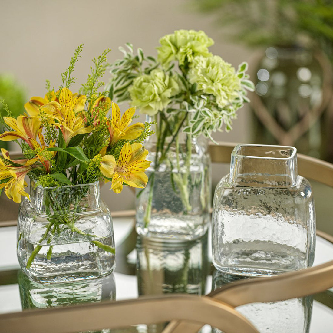 A collection of freshly cut flowers arranged in small, medium, and large Zodax Rippled Glass Vases on a glass table.