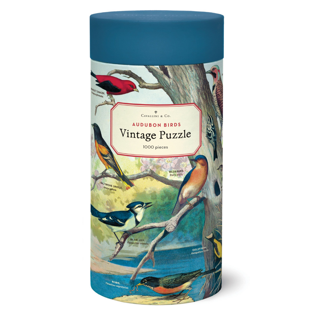 A cylindrical packaging of a Audubon bird puzzle with vintage illustrations. The box is predominantly blue and green with images of various birds, branches, and a label that reads &