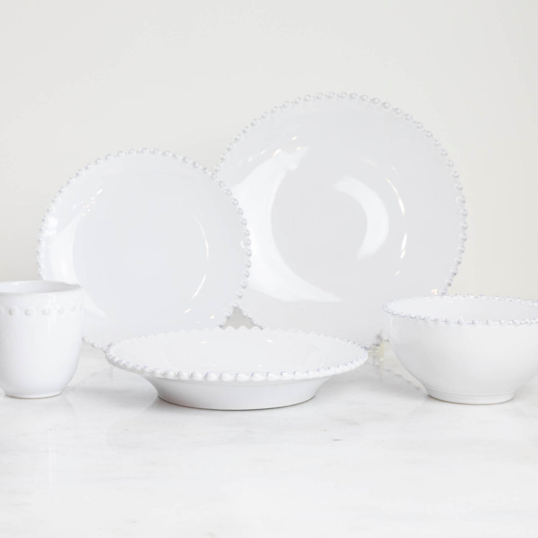 A set of Costa Nova Pearl White Dinnerware with beaded edge design displayed against a light background.