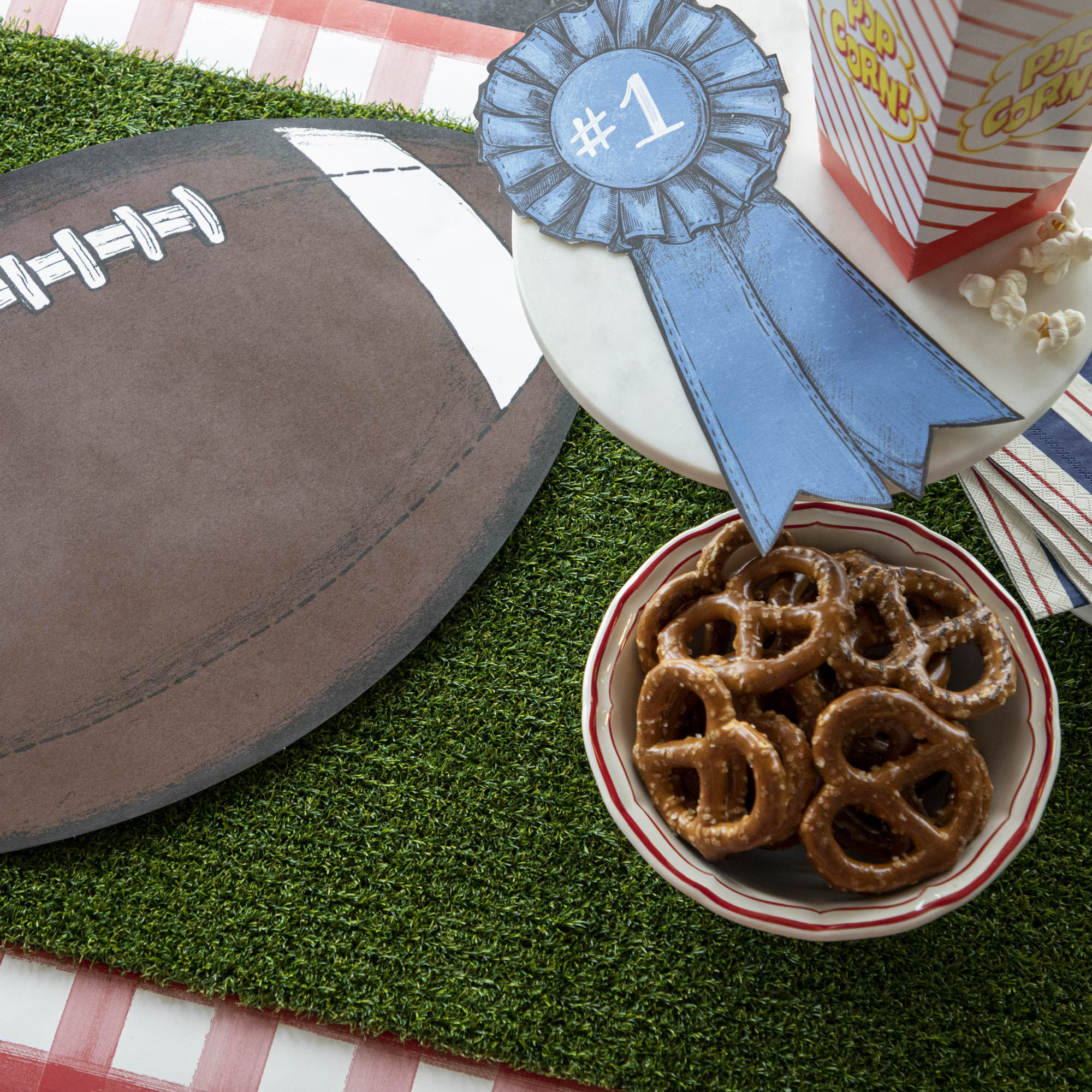 A bowl of pretzels and a football on a Talking Tables Artificial Grass Table Runner.