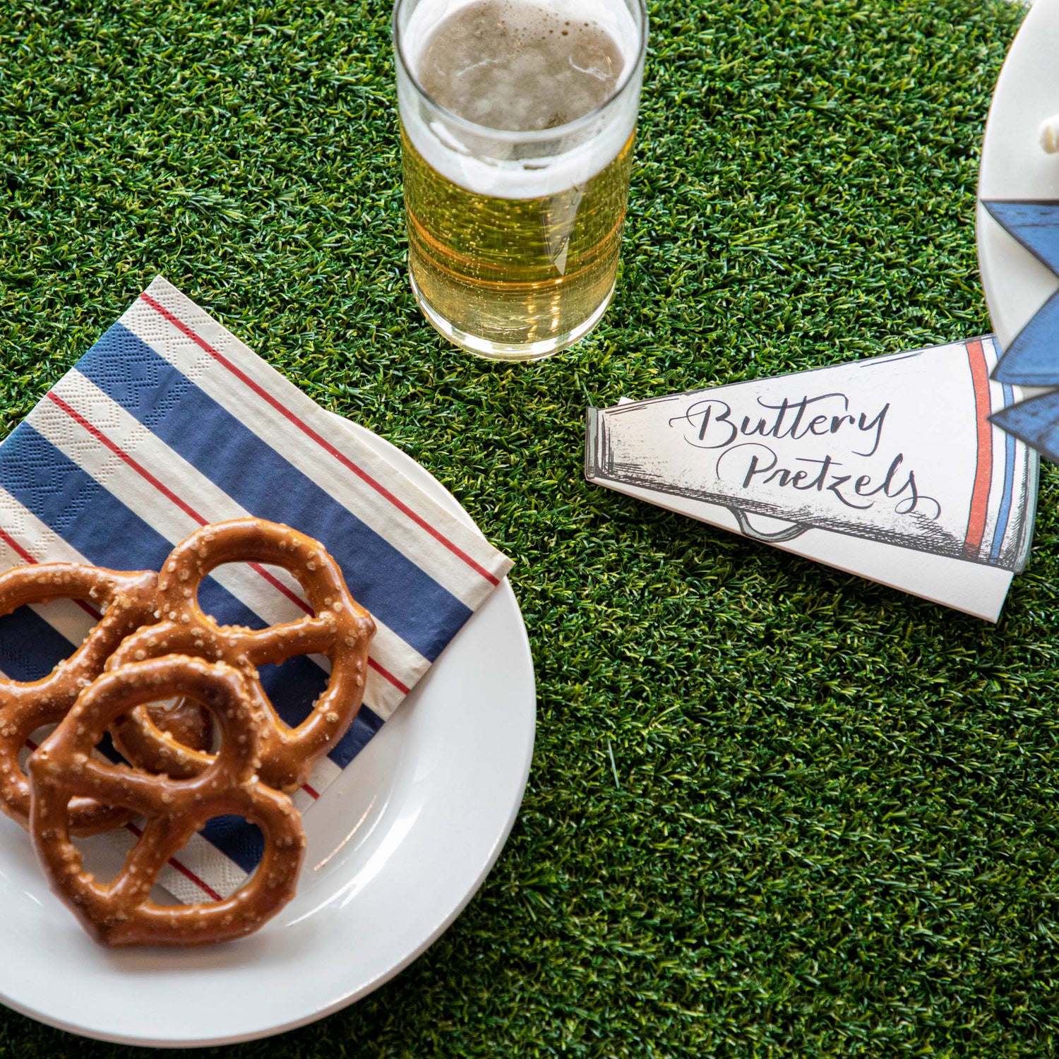 A Talking Tables Artificial Grass Table Runner with pretzels and beer on it.