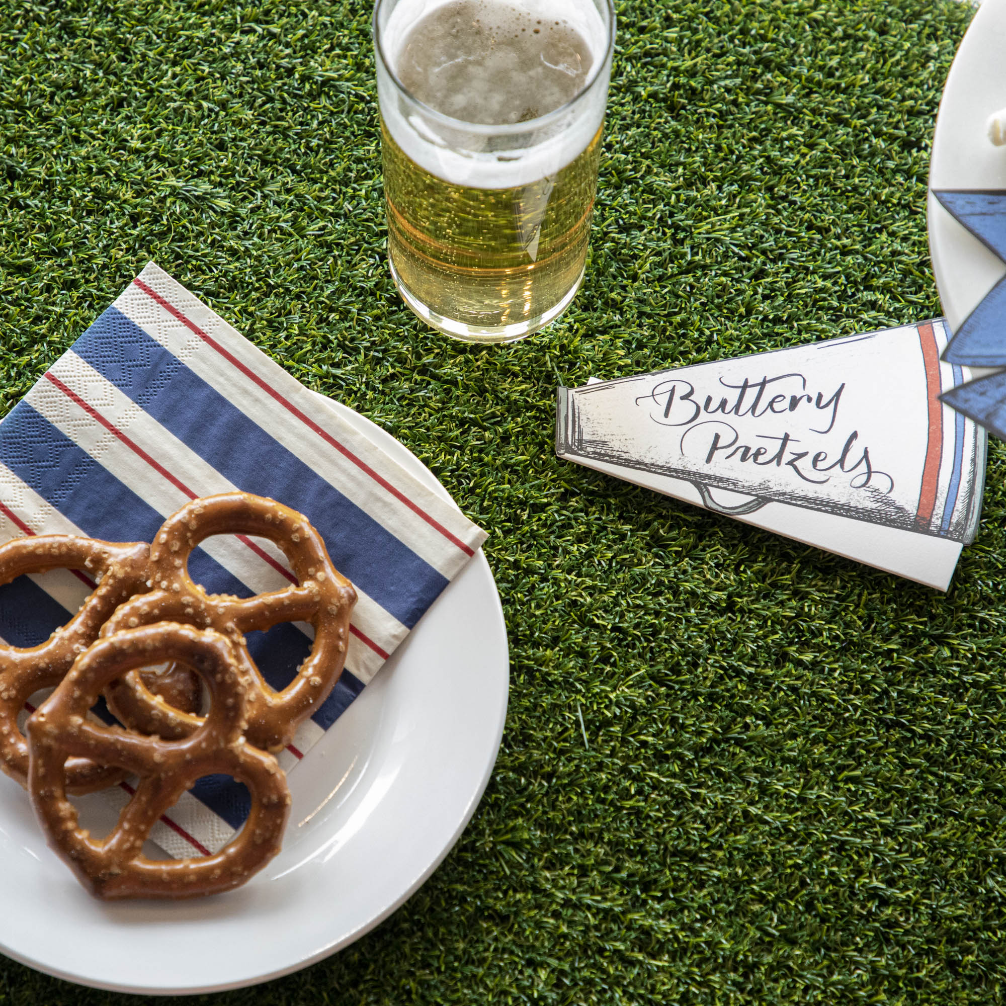 A Talking Tables Artificial Grass Table Runner with pretzels and beer on it.