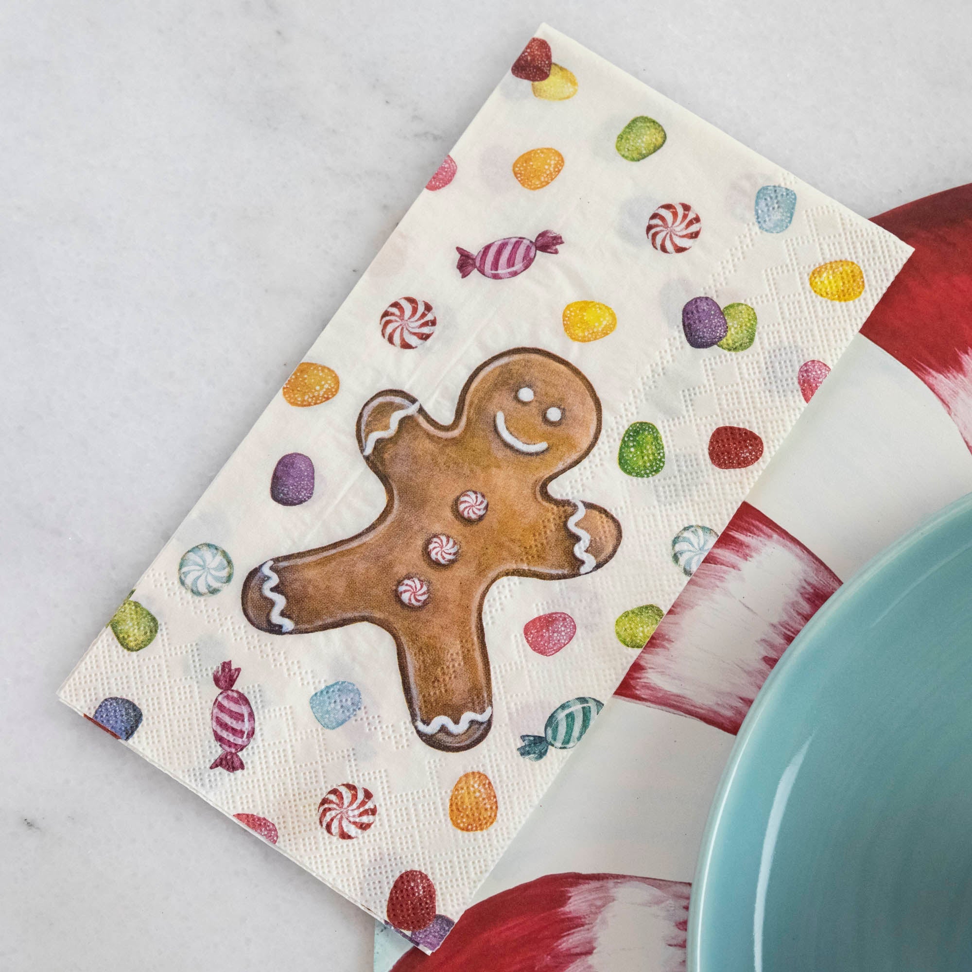 A Gingerbread Guest Napkin next to a plate in a Christmas candy-themed place setting.