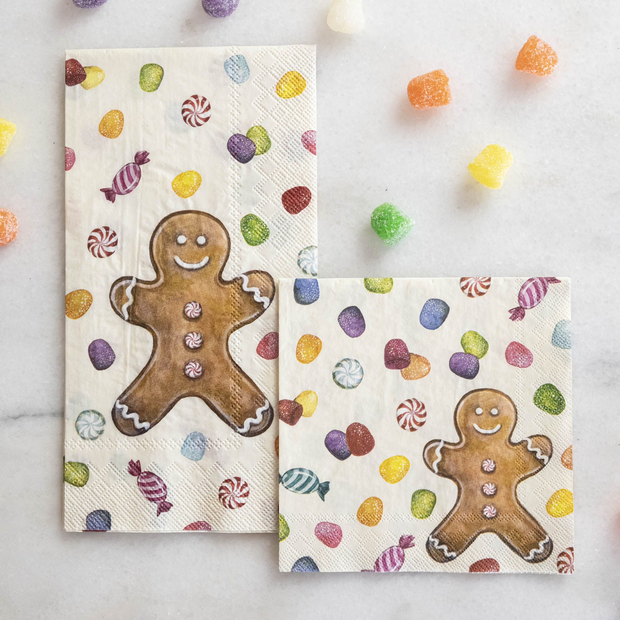 Two Gingerbread Napkins, one Guest and one Cocktail, on a white table surrounded by gumdrops.