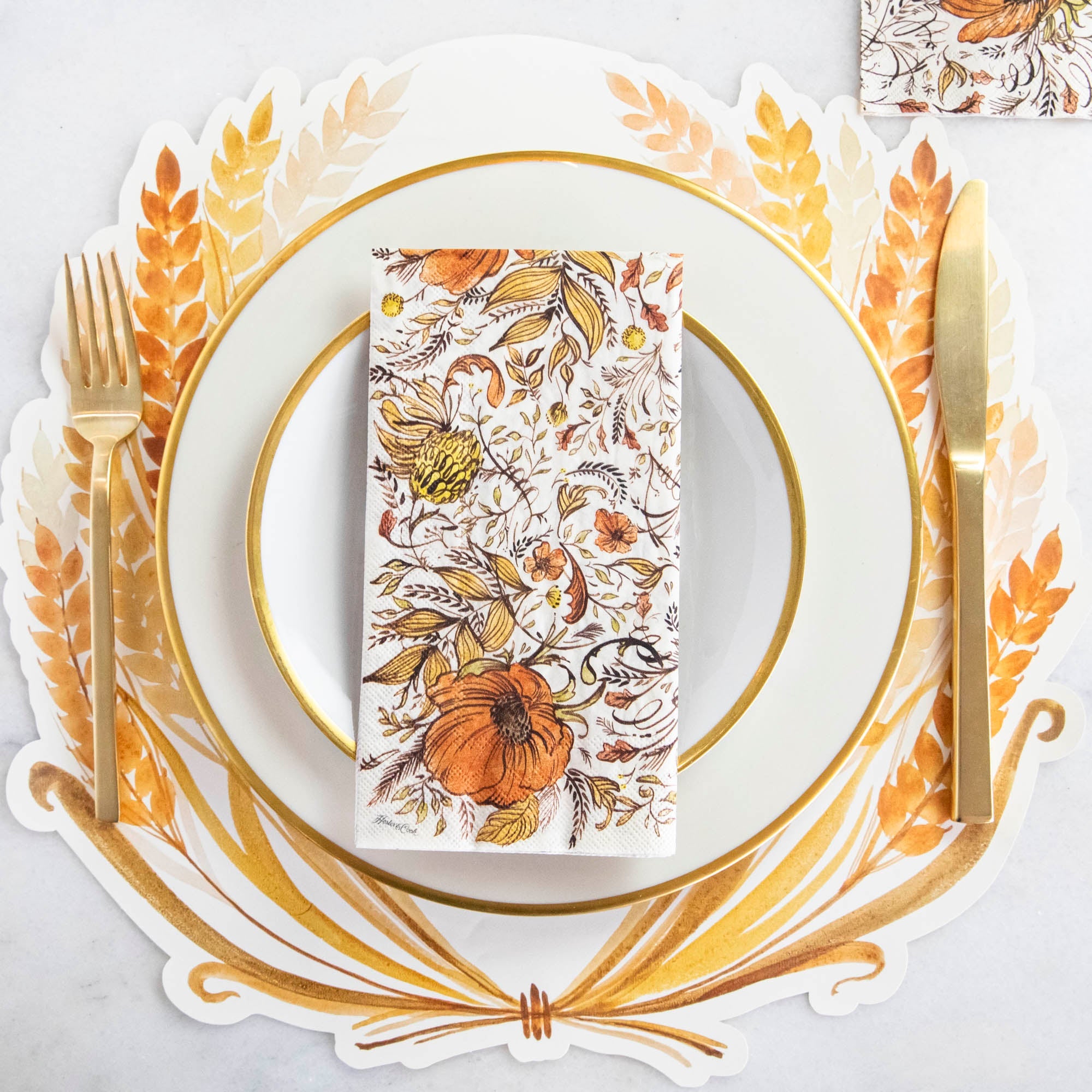 An Autumn Arrangement Guest Napkin on a gold-trimmed white plate in an elegant fall-themed place setting.