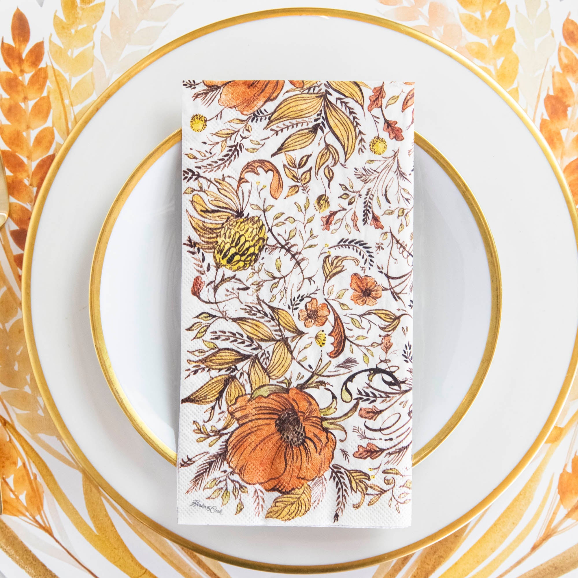 Close-up of an Autumn Arrangement Guest Napkin on a gold-trimmed white plate in an elegant fall-themed place setting.