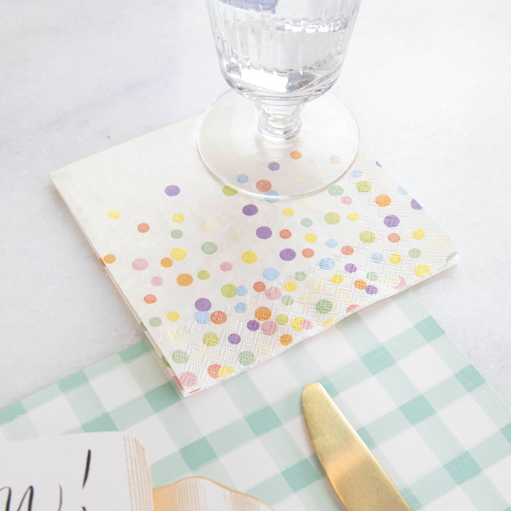 A Confetti Sprinkles Cocktail Napkin under a full water glass on an elegant place setting.