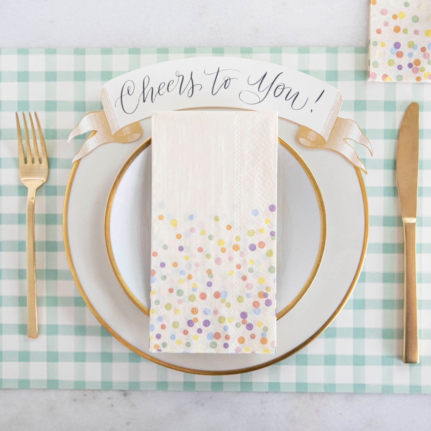 A Confetti Sprinkles Guest Napkin centered on a plate in a festive place setting, from above.