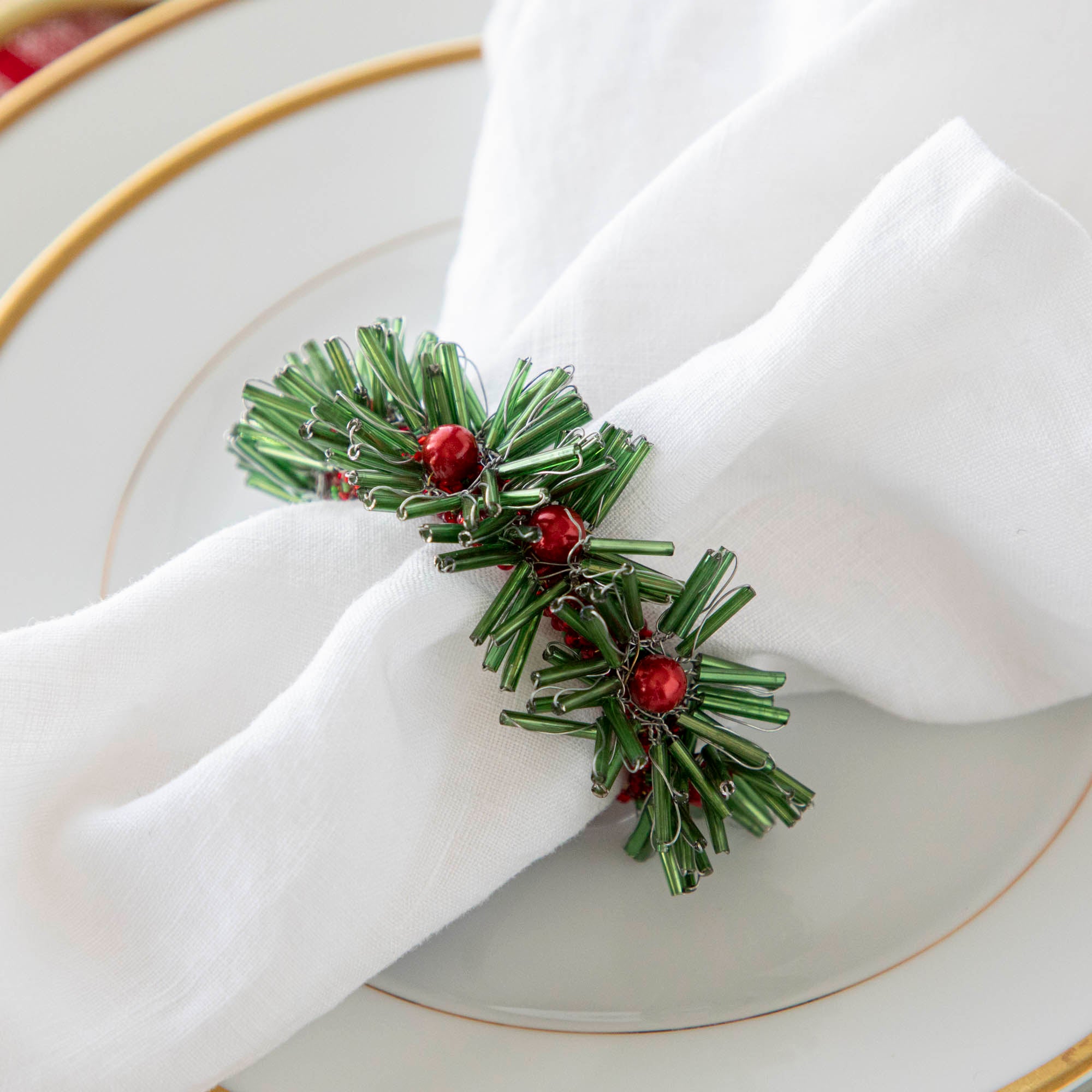 A close-up of a beaded green and red napkin ring on a white napkin.