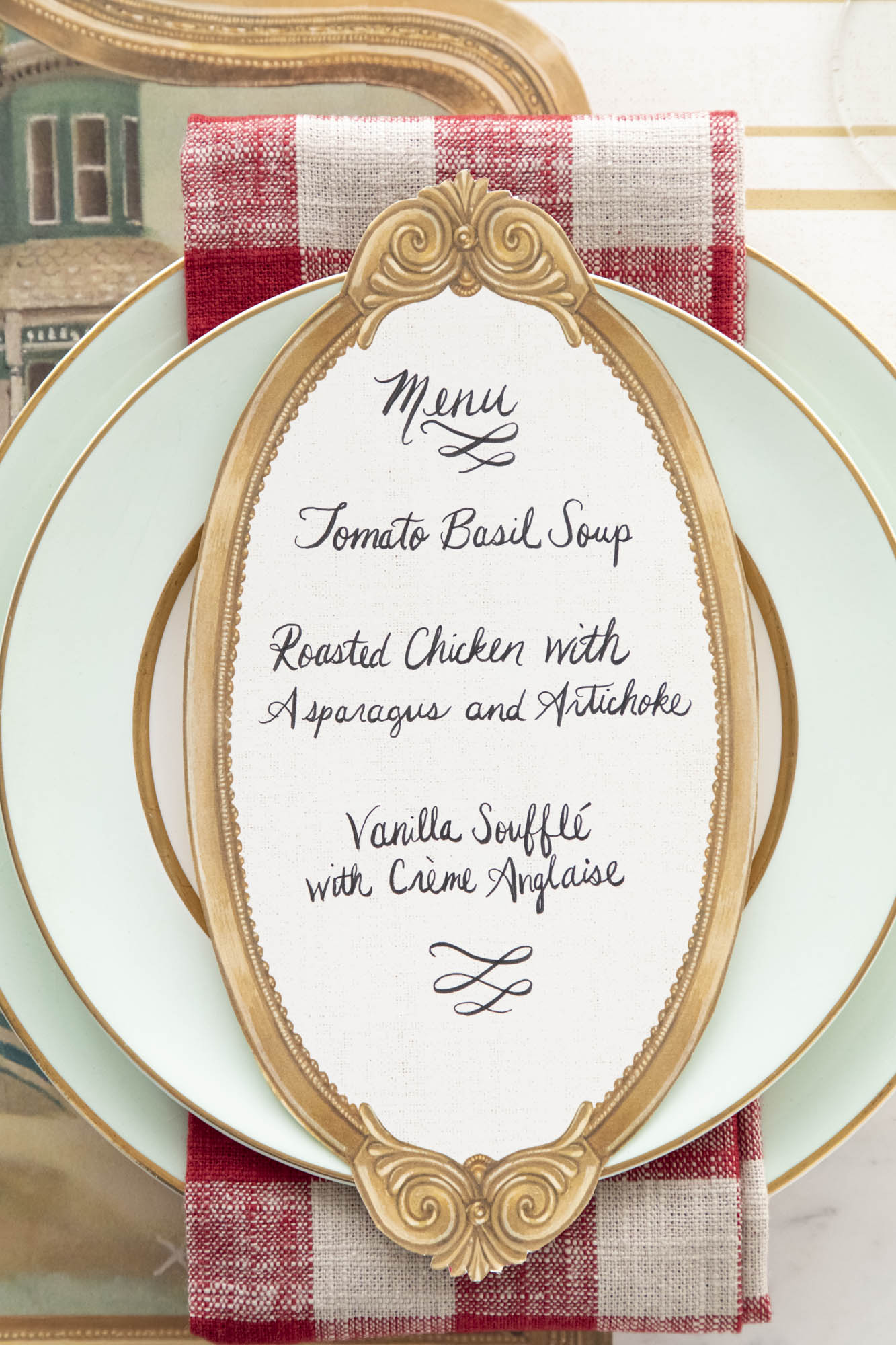 An Antique Gold Frame Table Card with a menu written on it in lovely cursive resting on the pate of an elegant place setting.