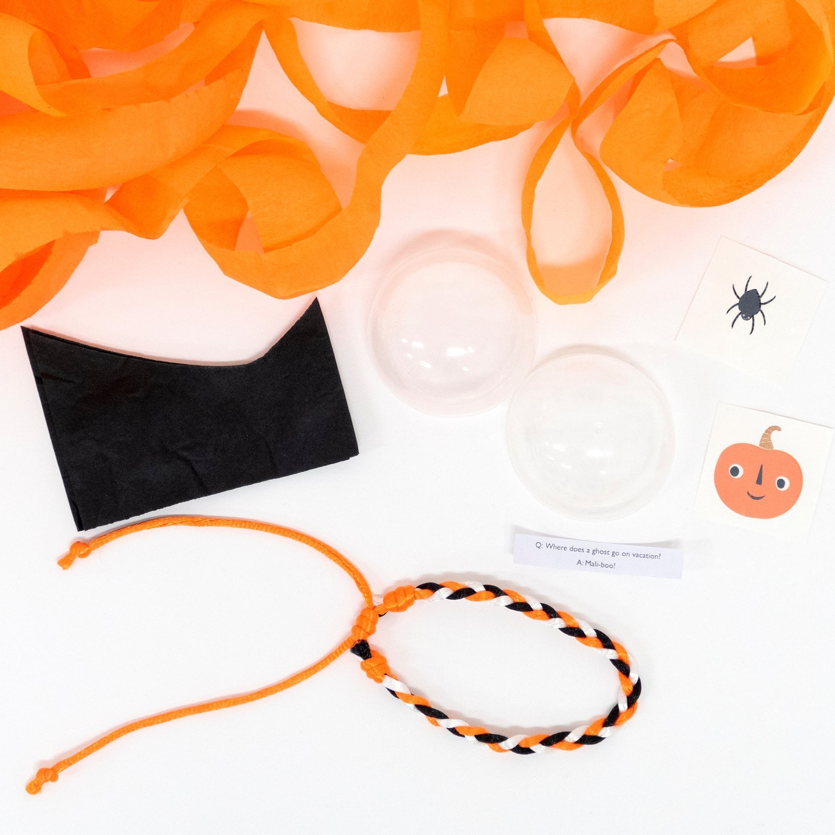 A friendship bracelet, in a plastic ball, 2 temporary tattoos with copper foil detail, a joke and a black tissue paper hat.