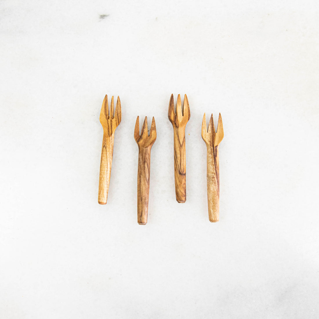 A set of Mini Olive Wood Appetizer Forks (Set of Four) from Natural Olivewood beside a piece of cheese on a wooden cutting board, ready for hors d&