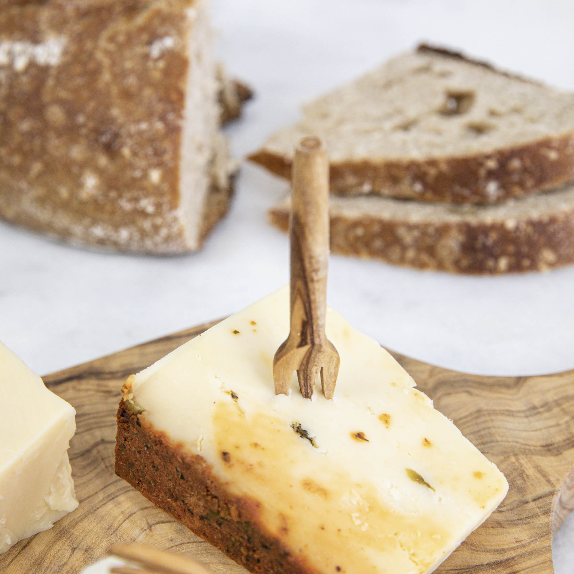 A set of Mini Olive Wood Appetizer Forks (Set of Four) from Natural Olivewood beside a piece of cheese on a wooden cutting board, ready for hors d&