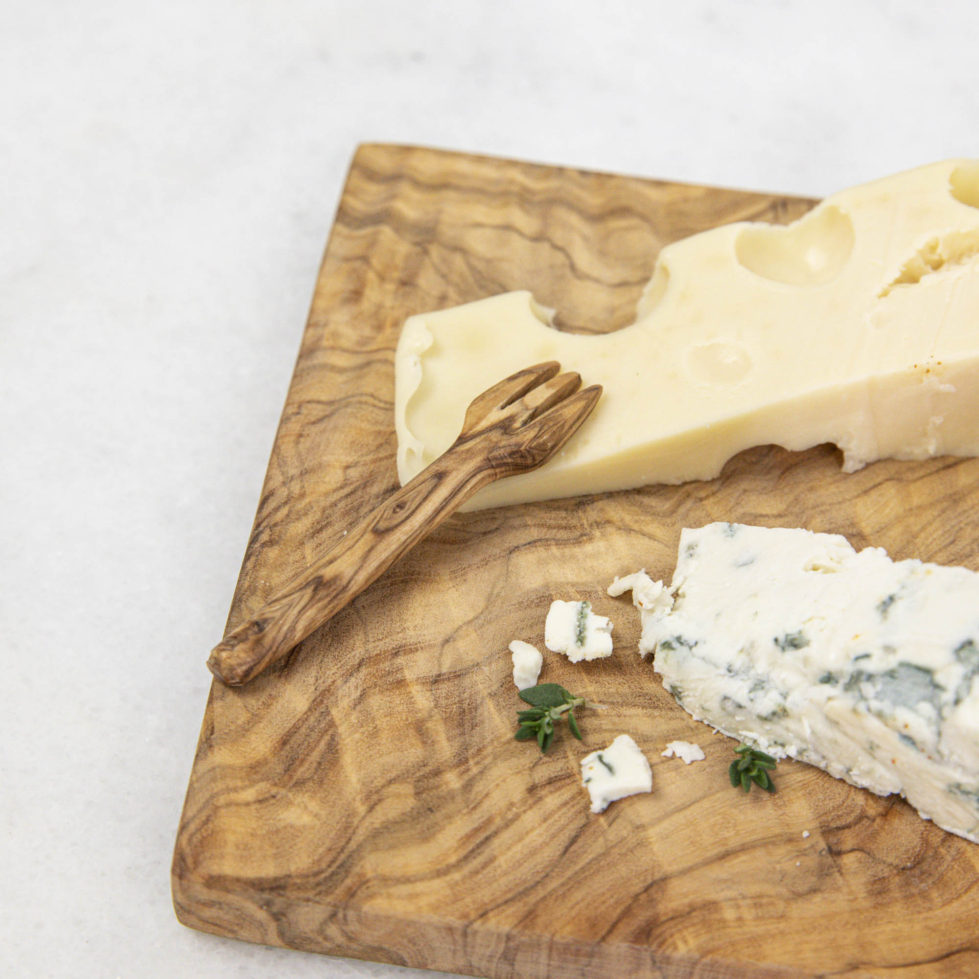 A set of Mini Olive Wood Appetizer Forks (Set of Four) from Natural Olivewood beside a piece of cheese on a wooden cutting board, ready for hors d&