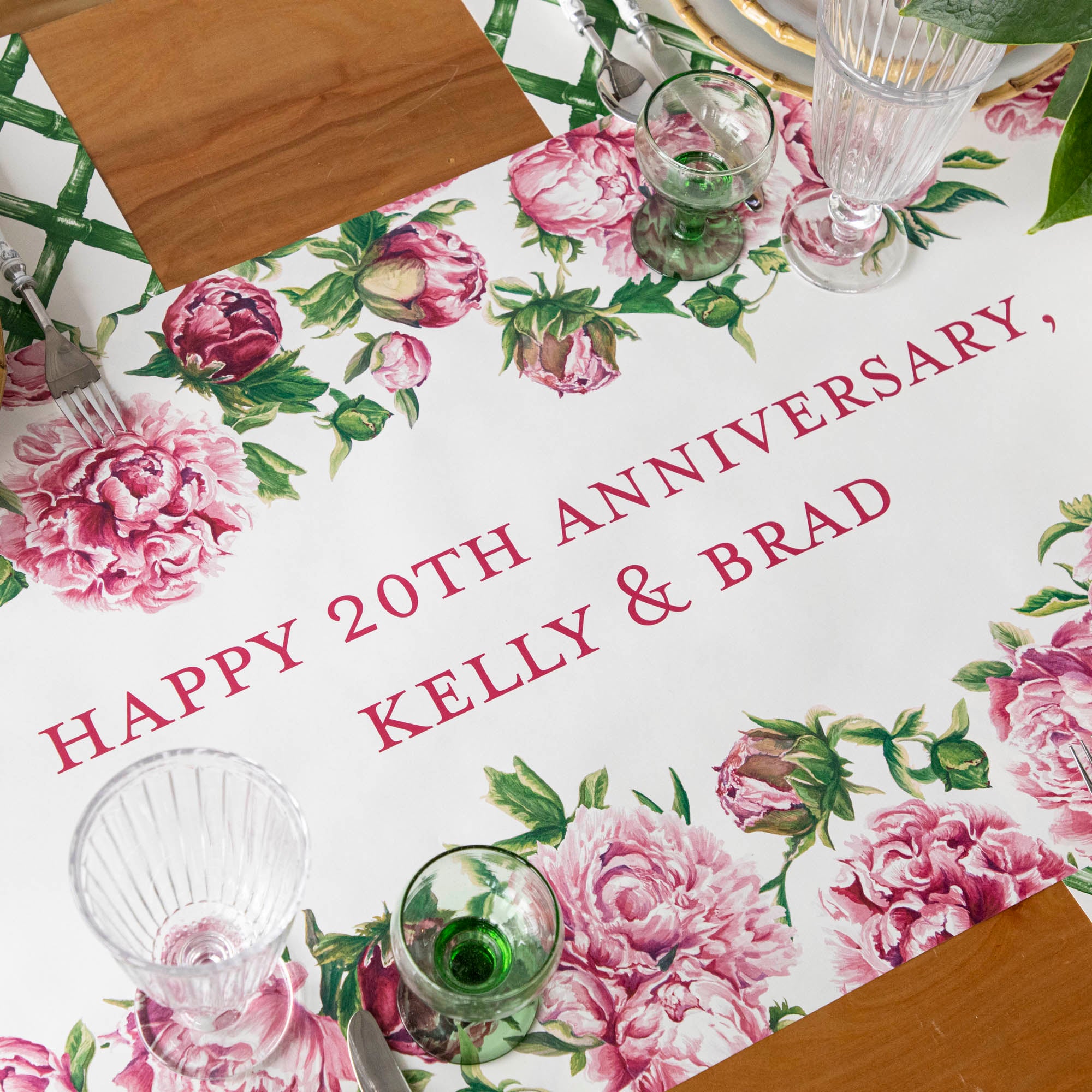 The Peony Personalized Runner, with "HAPPY 20TH ANNIVERSARY, KELLY & BRAD" printed down the middle in dark pink, under an elegant table setting.