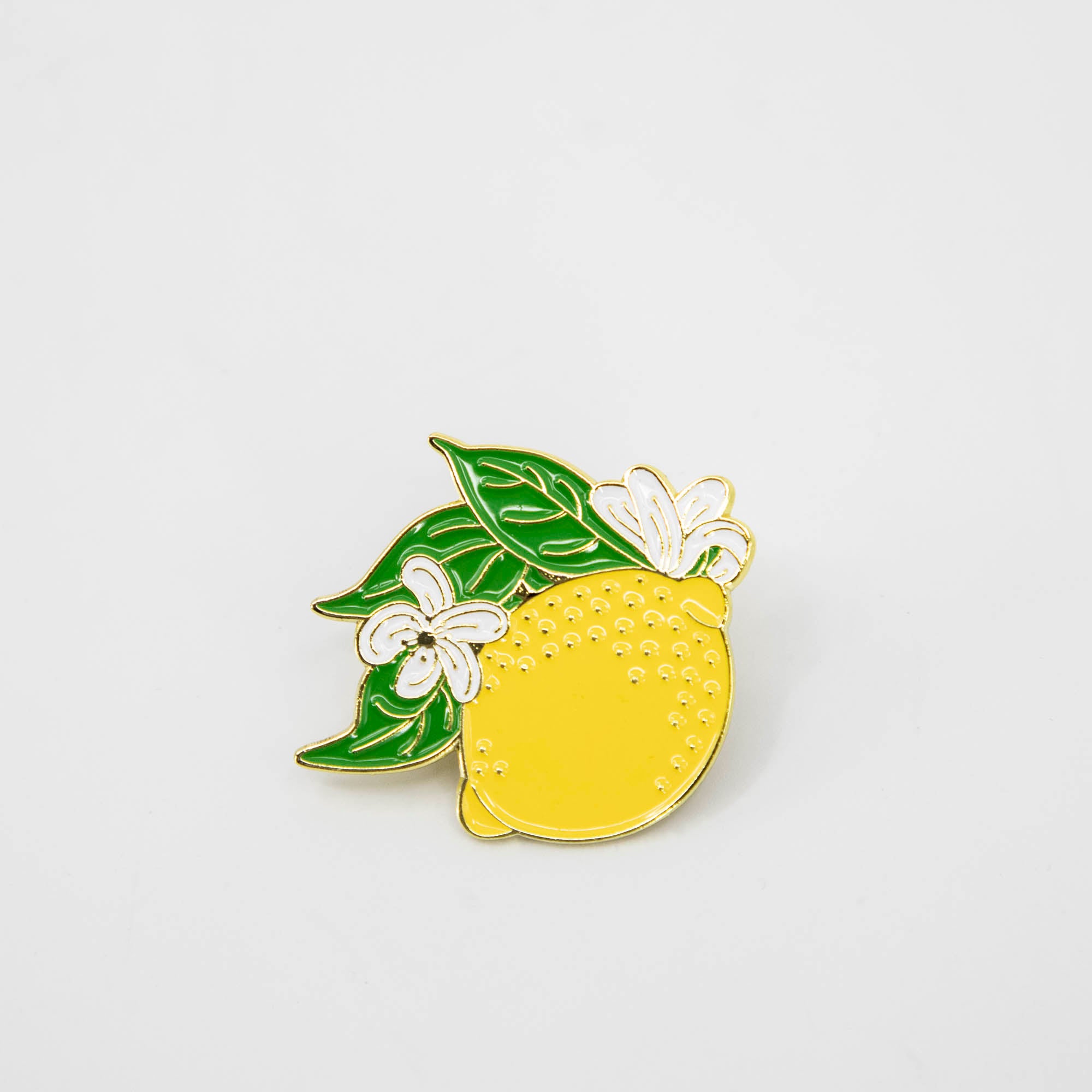 A vibrant Hester & Cook Lemon Enamel Pin adorned with lush leaves that embodies the freshness of citrus fruits.