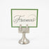 An elegant, silver, short round stand topped by a flat card-holder with two flat prongs, holding a place card reading "Francis".