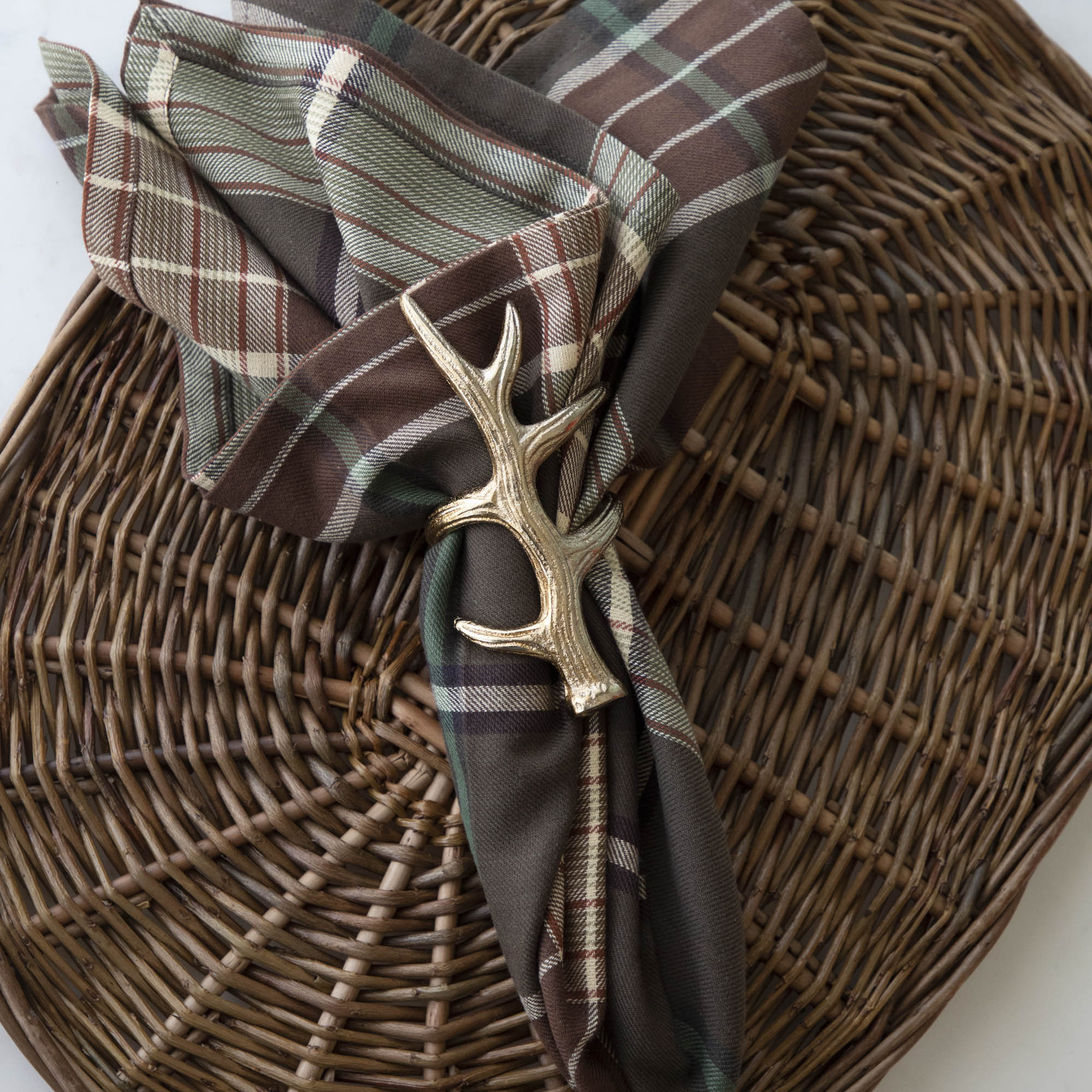 A napkin ring featuring an antler design, placed on a woven mat, with a checkered napkin inserted.