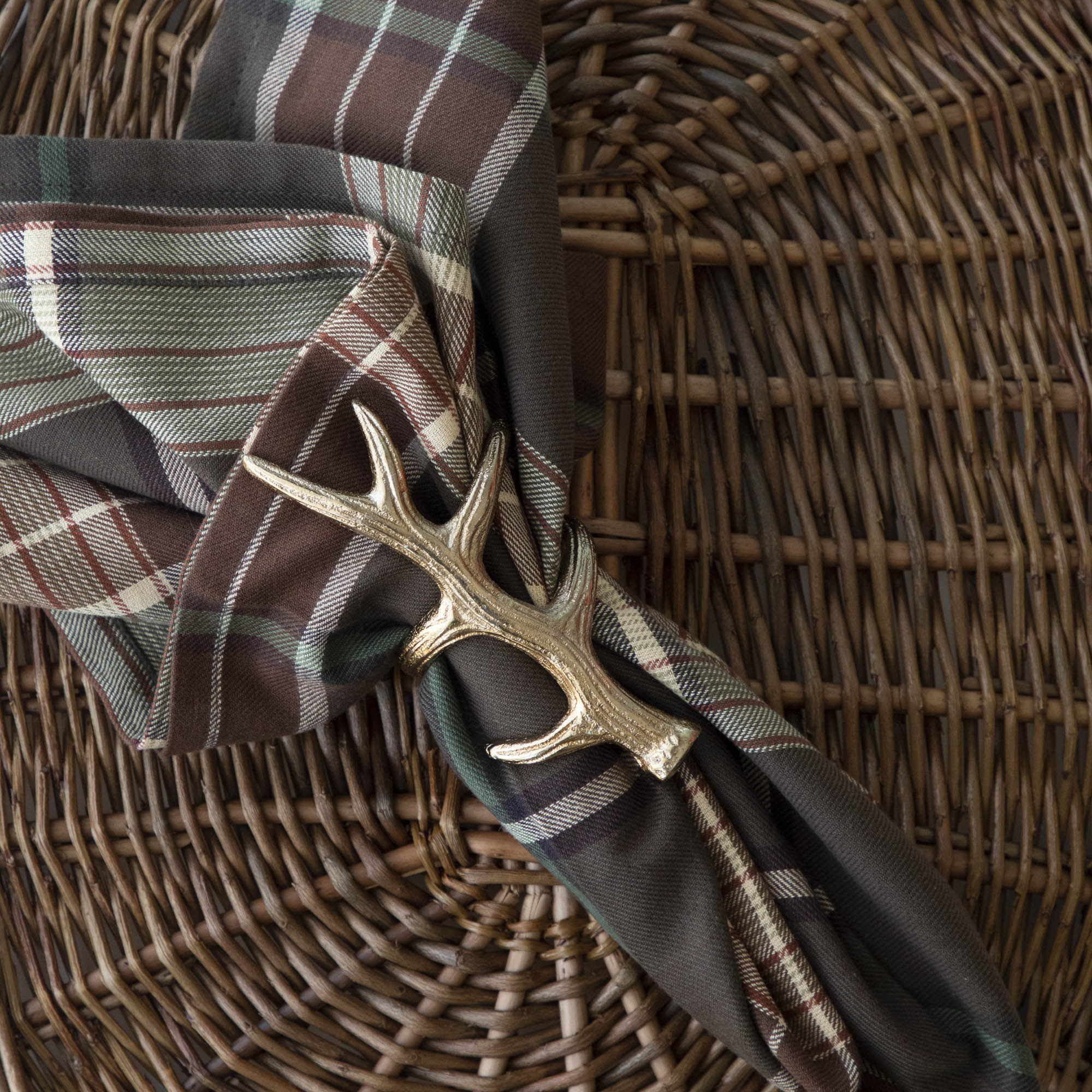 A napkin ring featuring an antler design, placed on a woven background with a brown plaid napkin inserted.