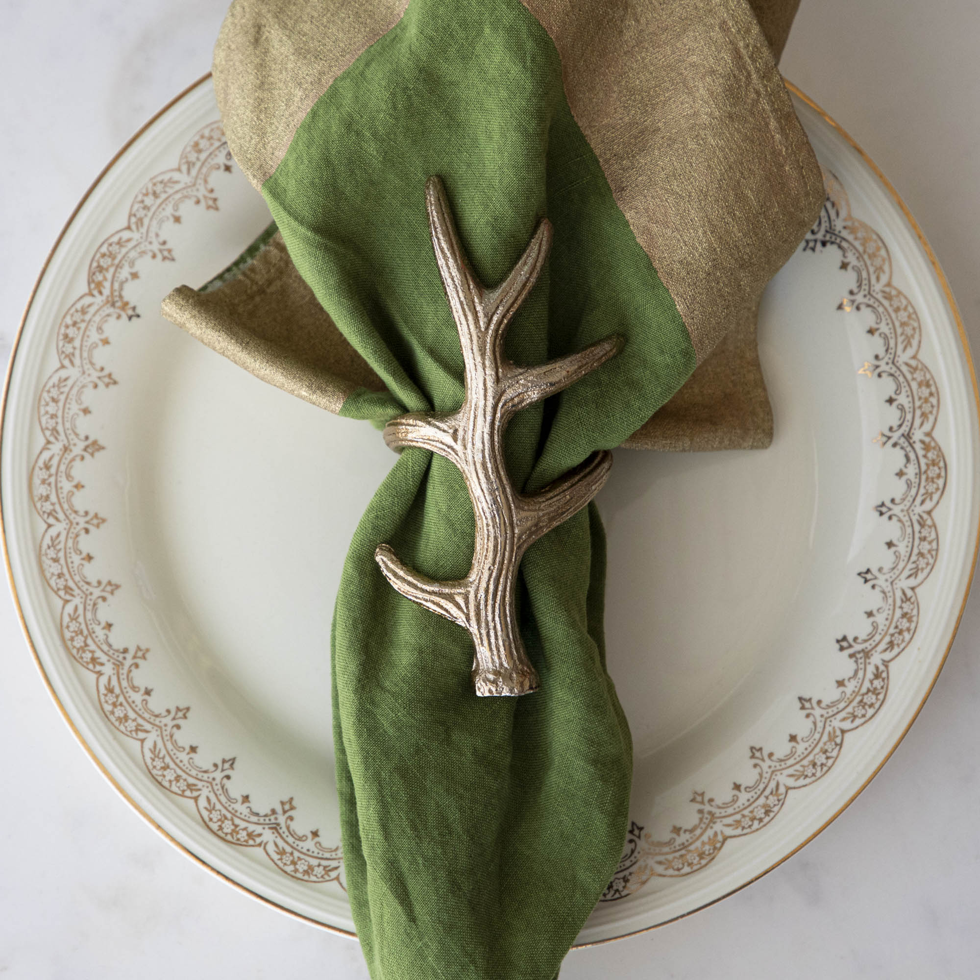 A napkin ring featuring an antler design, placed on a white plate with a green napkin inserted.