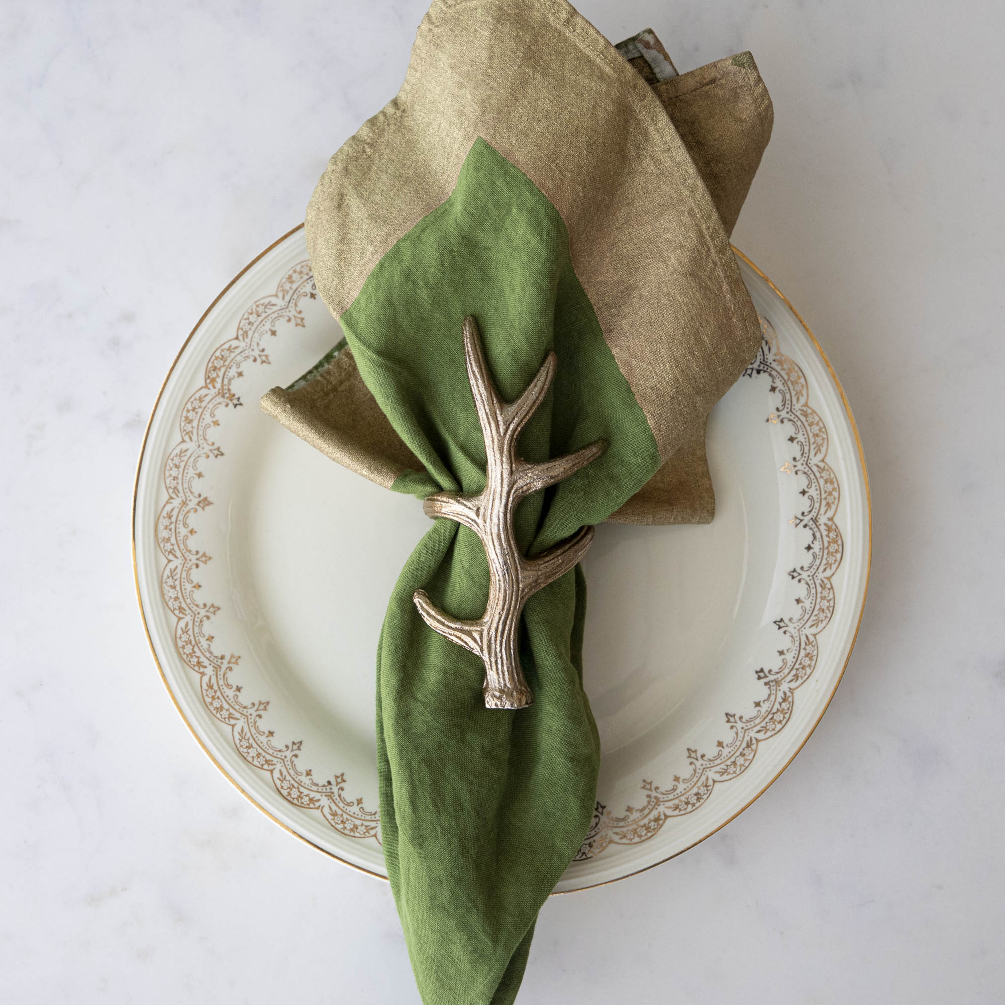 A napkin ring featuring an antler design, placed on a white plate with a green napkin inserted.