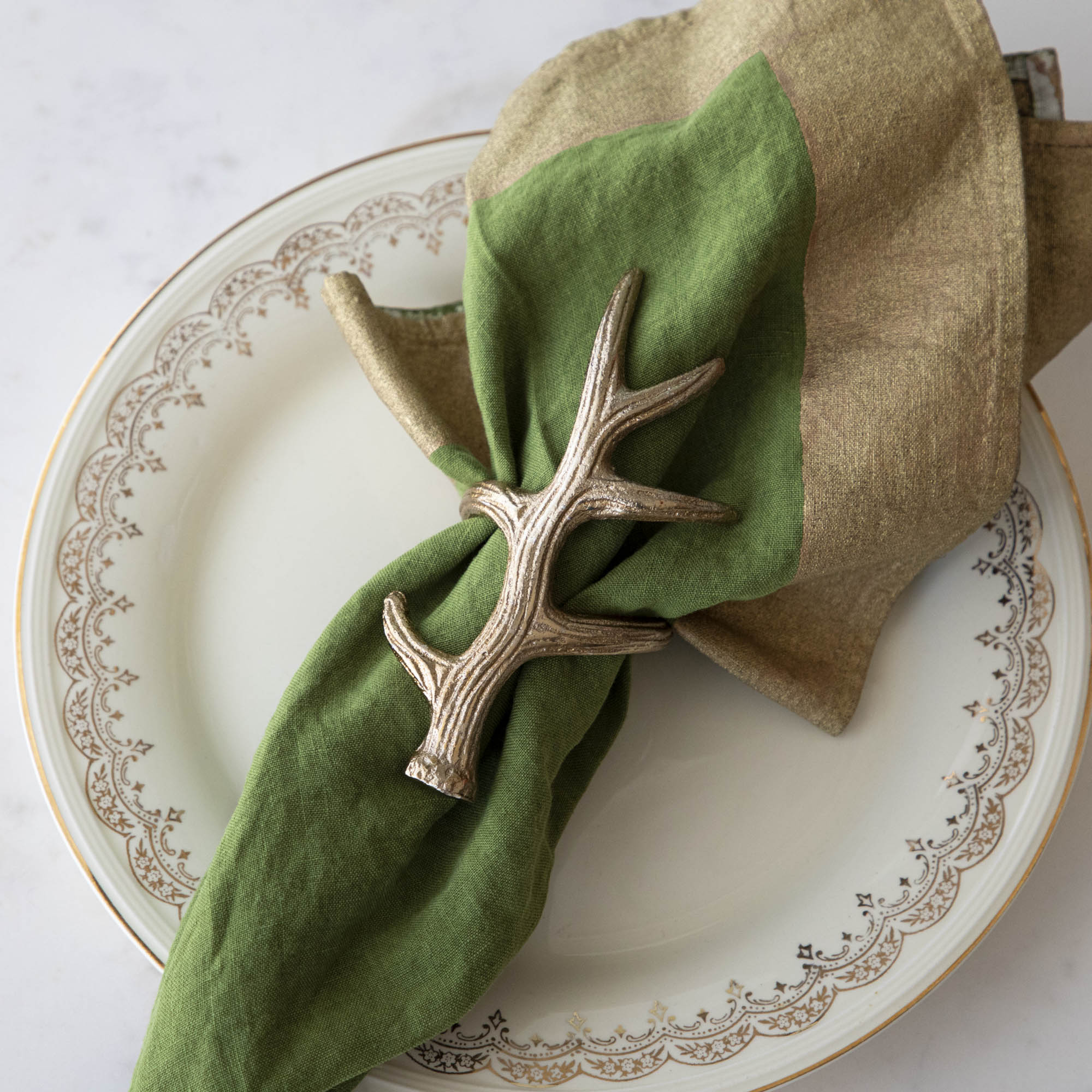 A napkin ring featuring an antler design, placed on a white plate with a green napkin inserted.