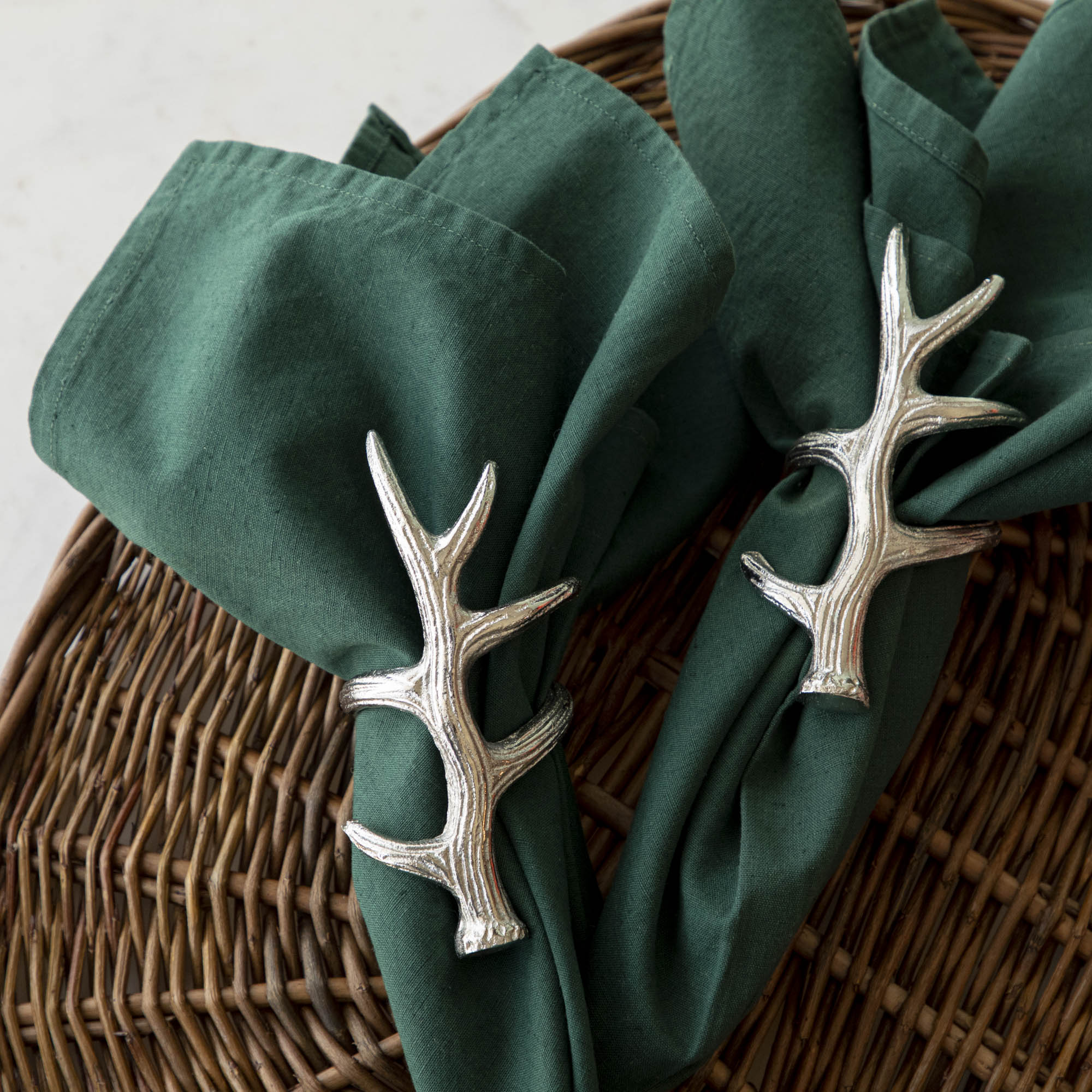 A napkin ring featuring an antler design, placed on a woven background with a green napkin inserted.